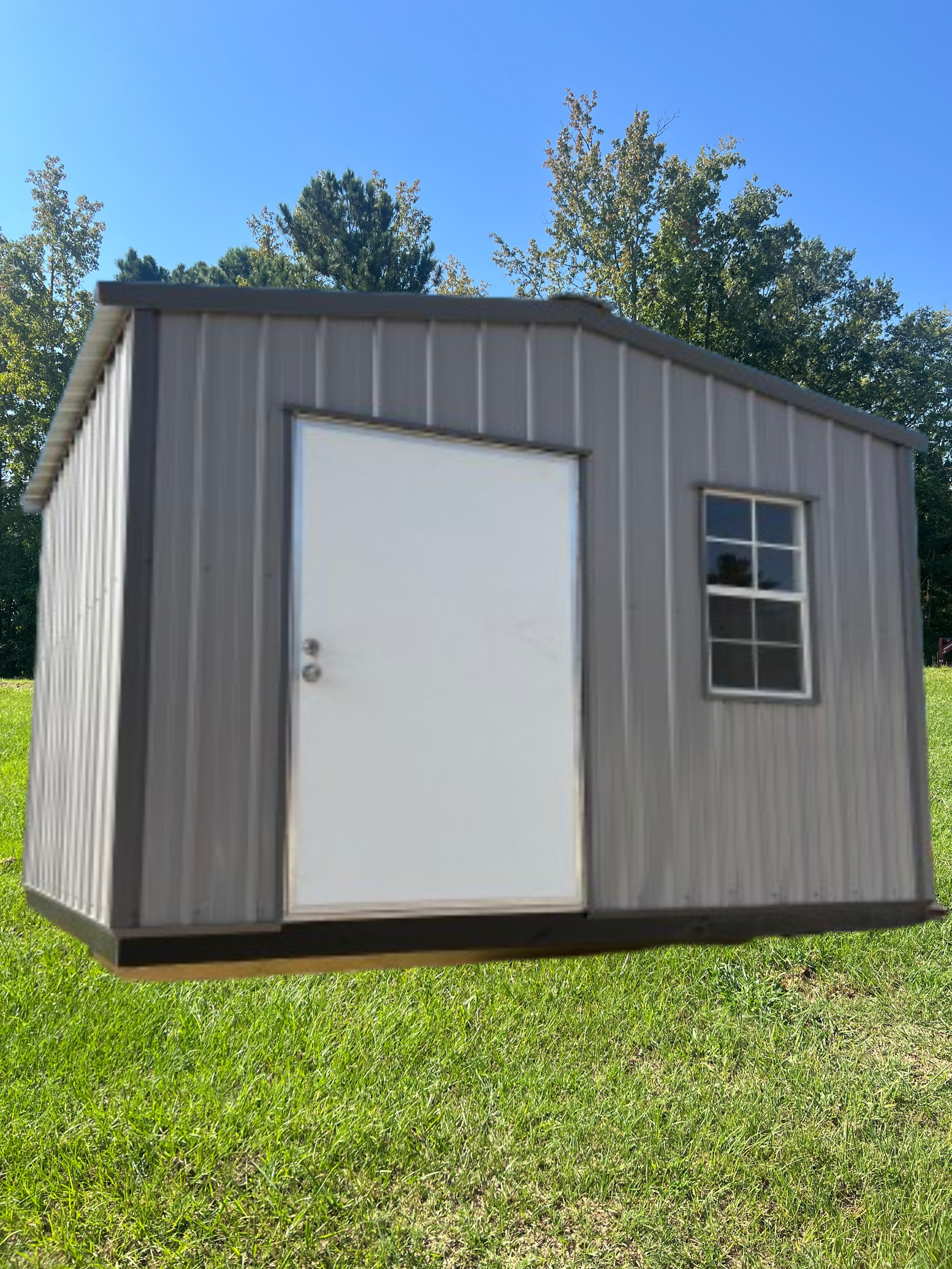 A grey metal storage shed with a single white door and one window, set on a grassy hill under a clear blue sky.
