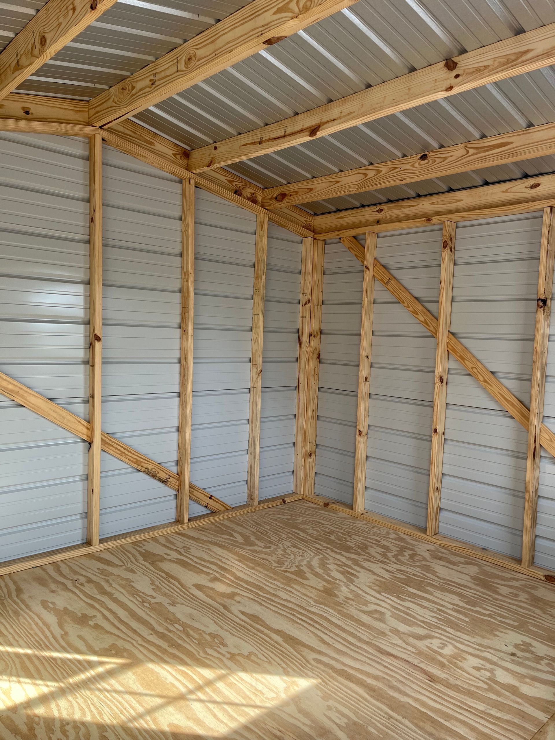Empty metal and wood shed interior with plywood floor and sunlight on the floor