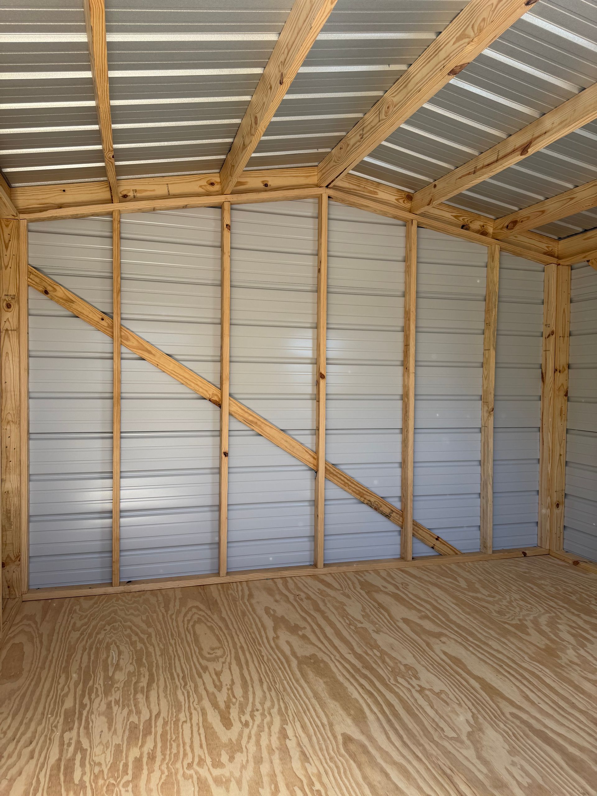 Empty wooden shed interior with exposed framing, metal roof, and plywood floor.