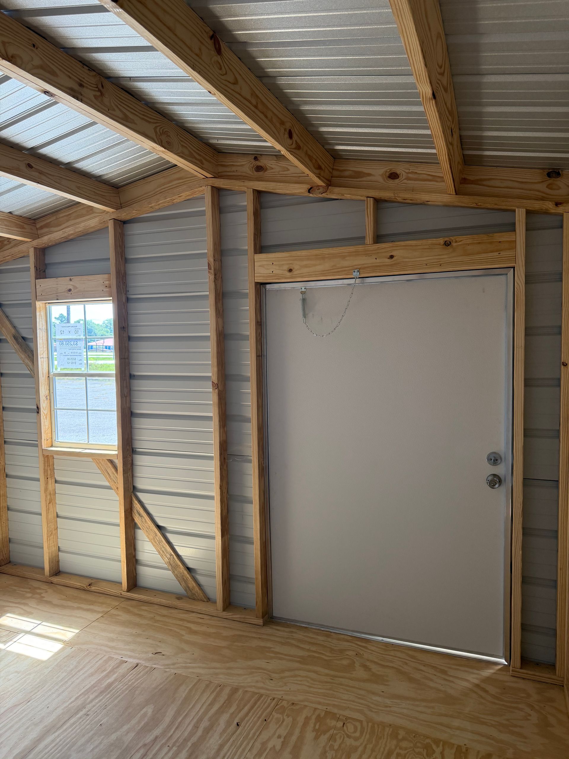 Interior of unfinished shed with exposed framing, corrugated walls, small window, and closed white door