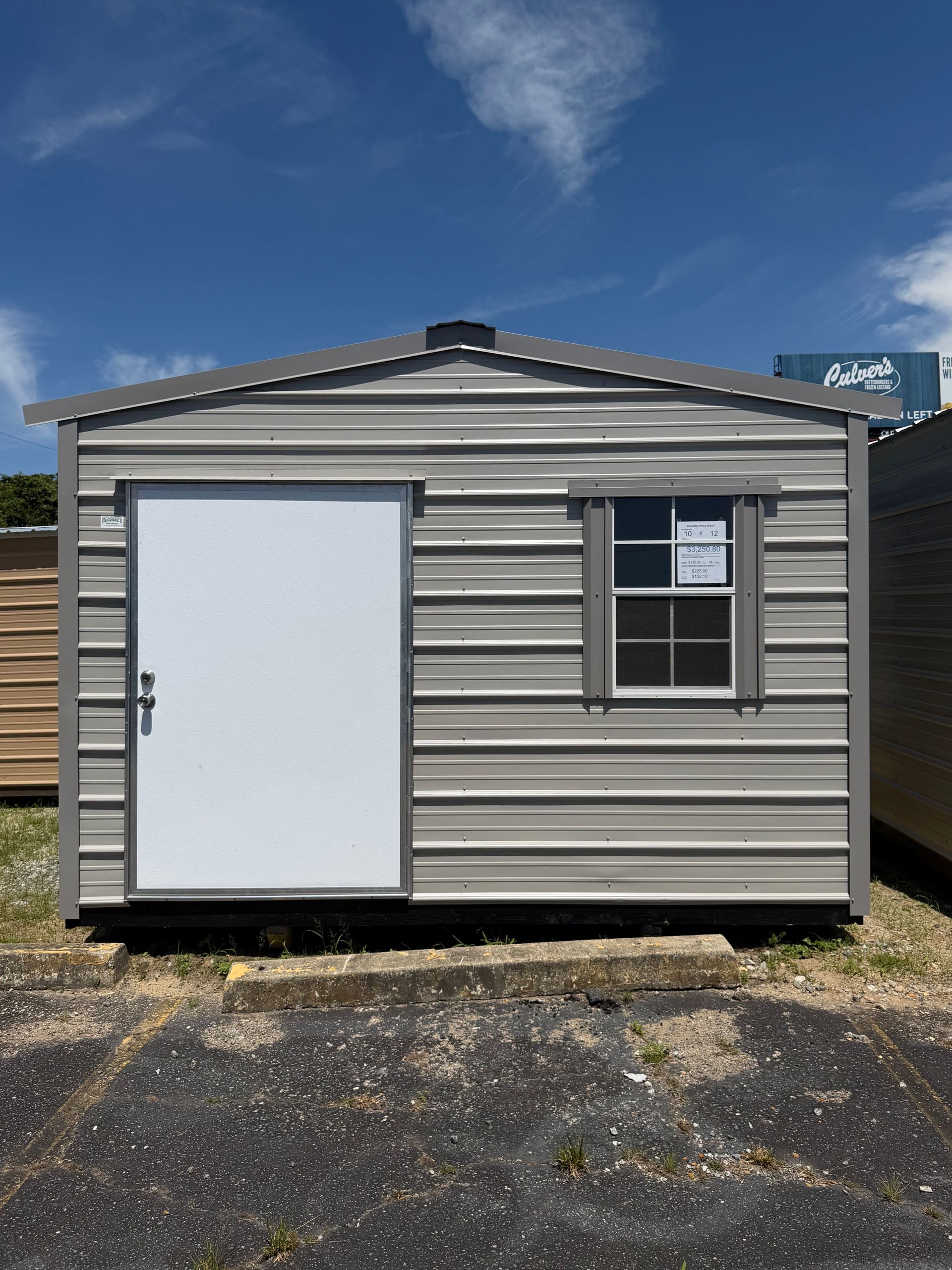 Small gray portable building with white door and window, sitting on gravel under a blue sky