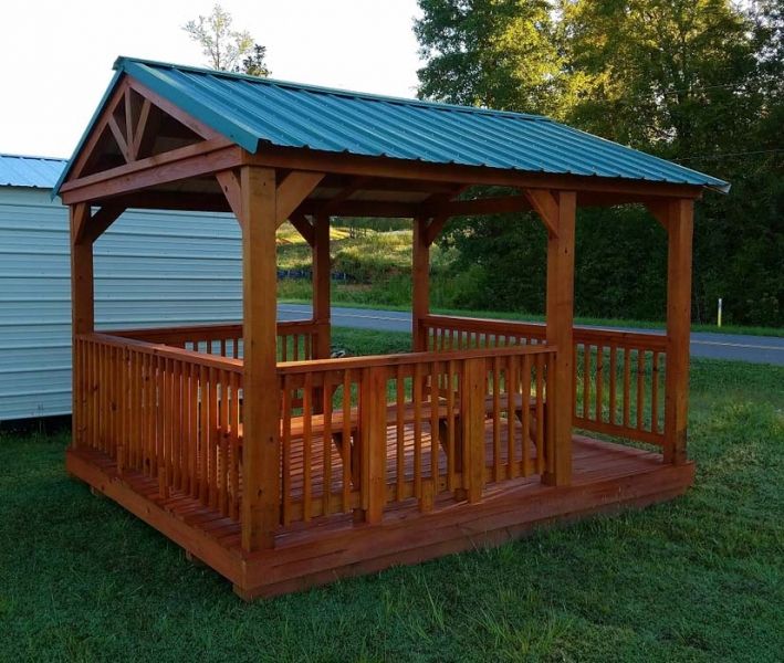 Wooden gazebo with a green metal roof, set on a deck, with a small picnic table inside.