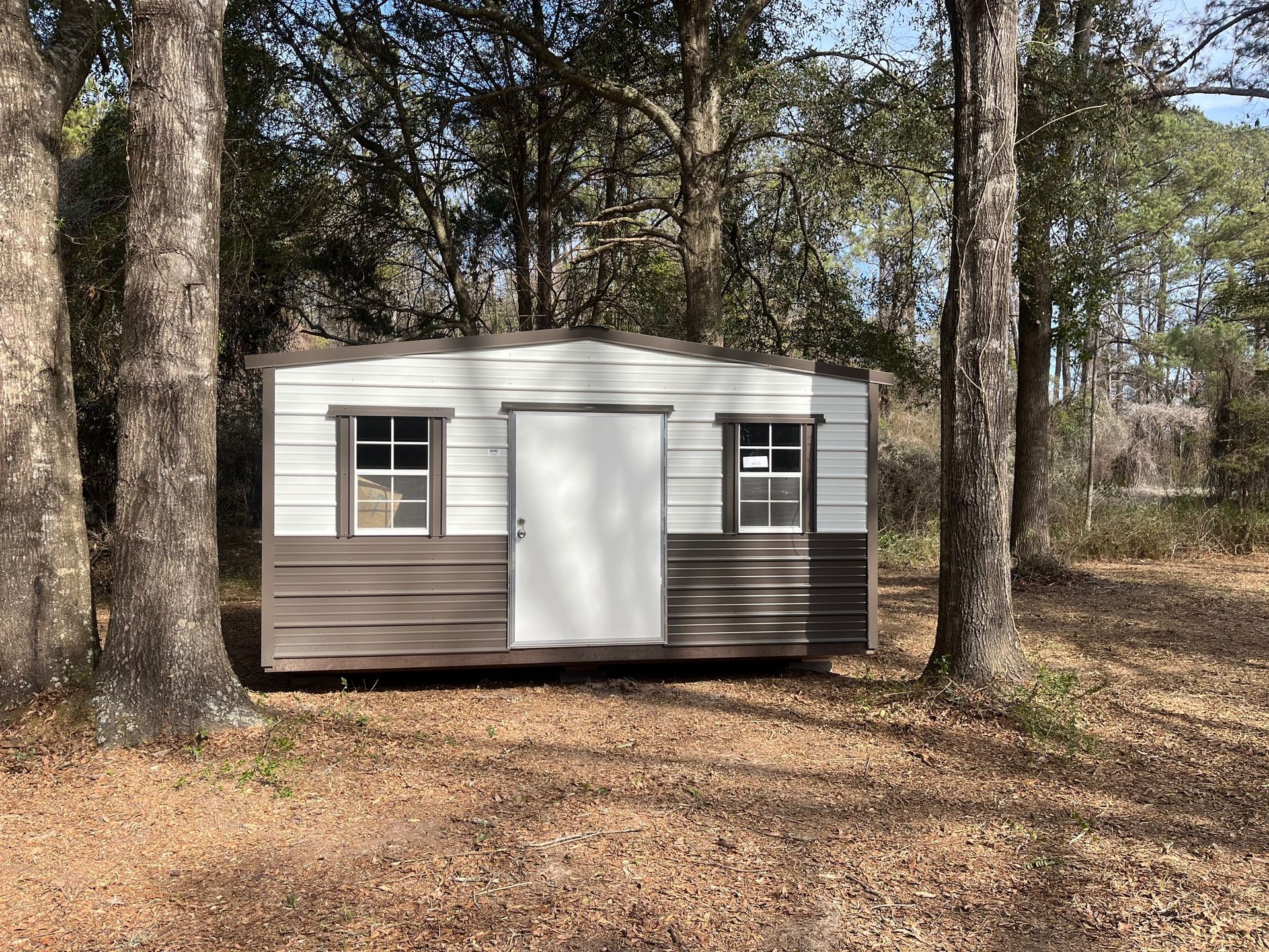 Metal shed with a white door and two small windows, in a wooded area.