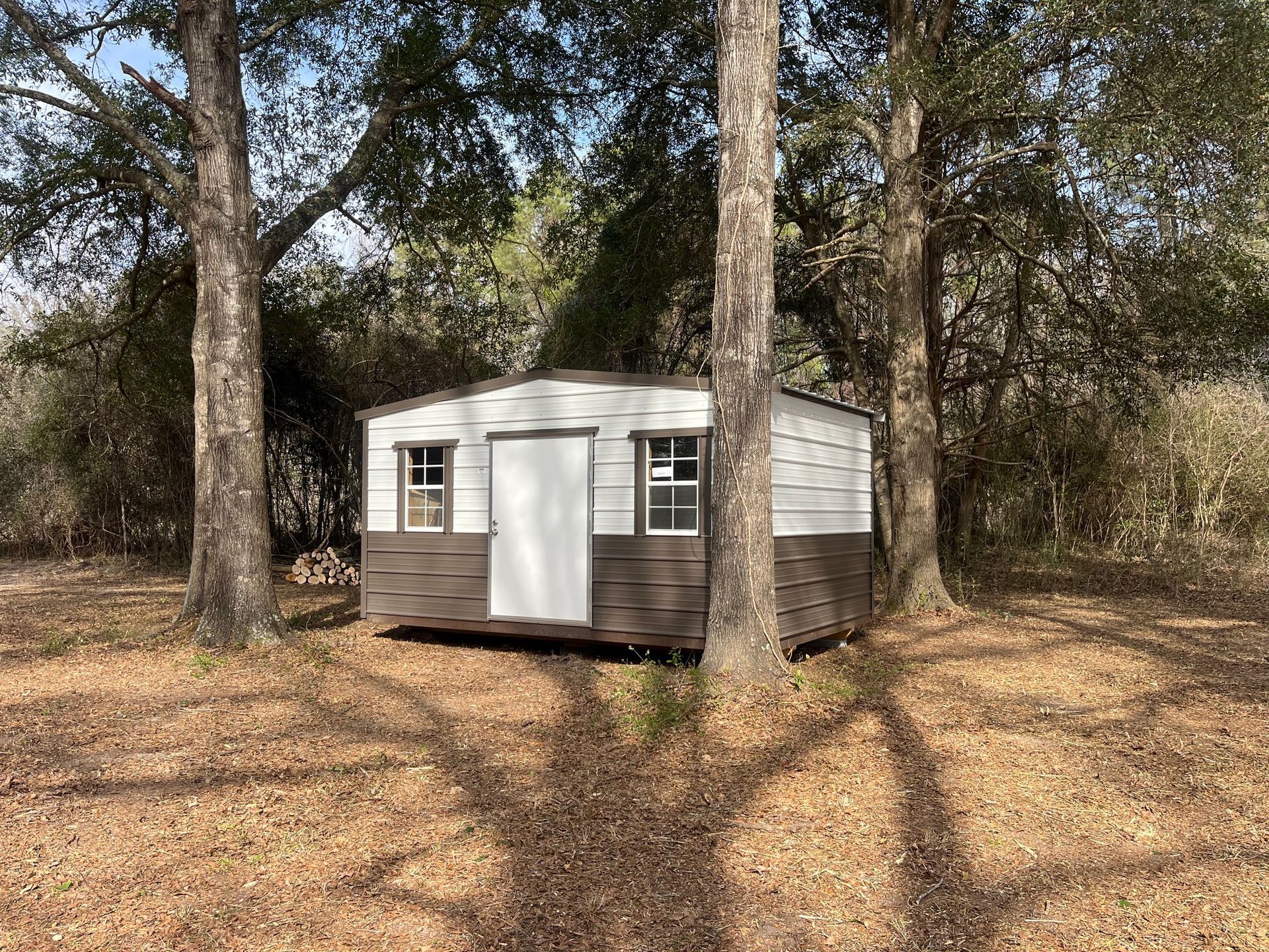 Small metal shed, white and brown, among trees in a wooded area.