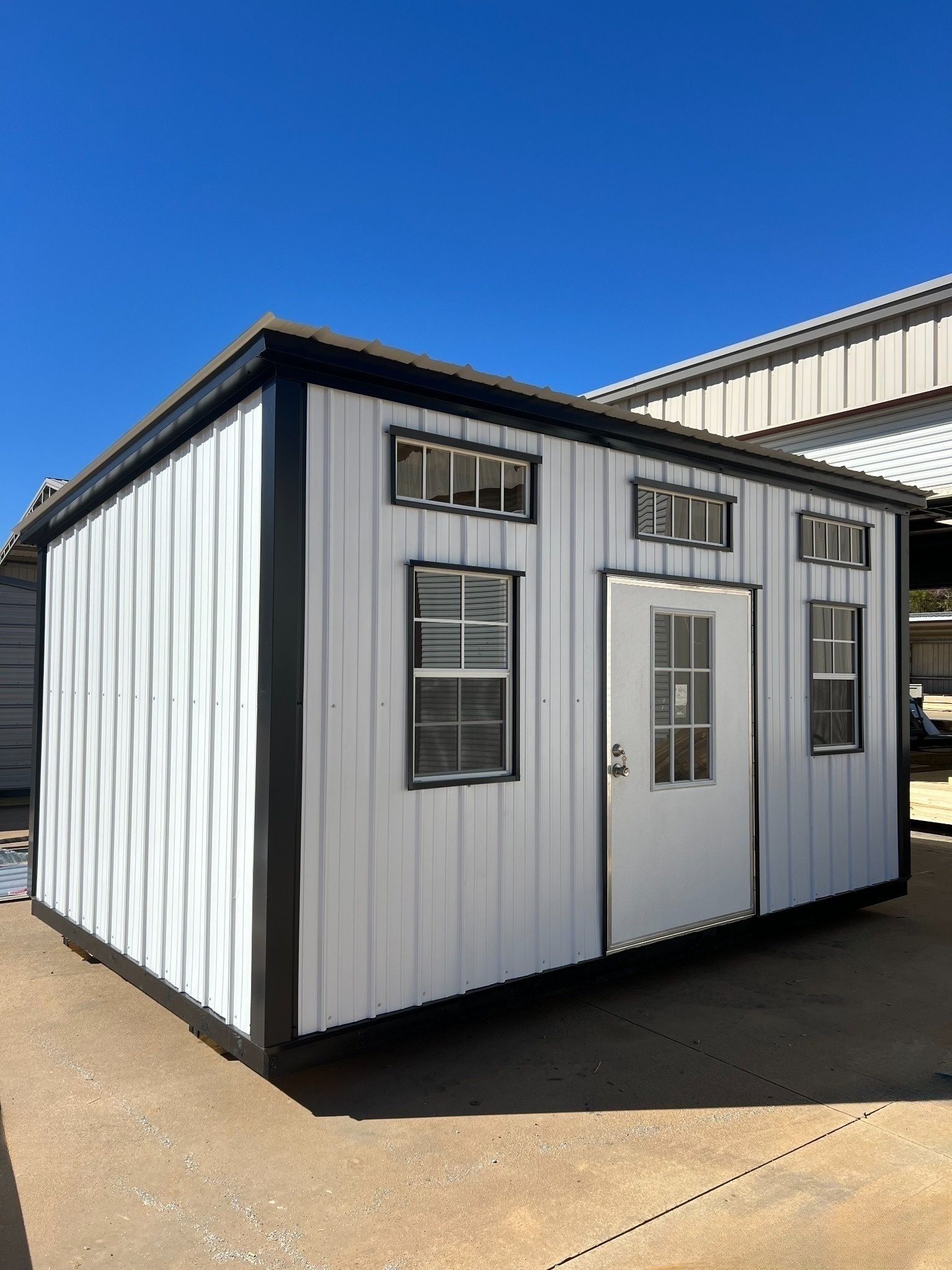 White tiny home with black trim and door, windows, on a sunny day.