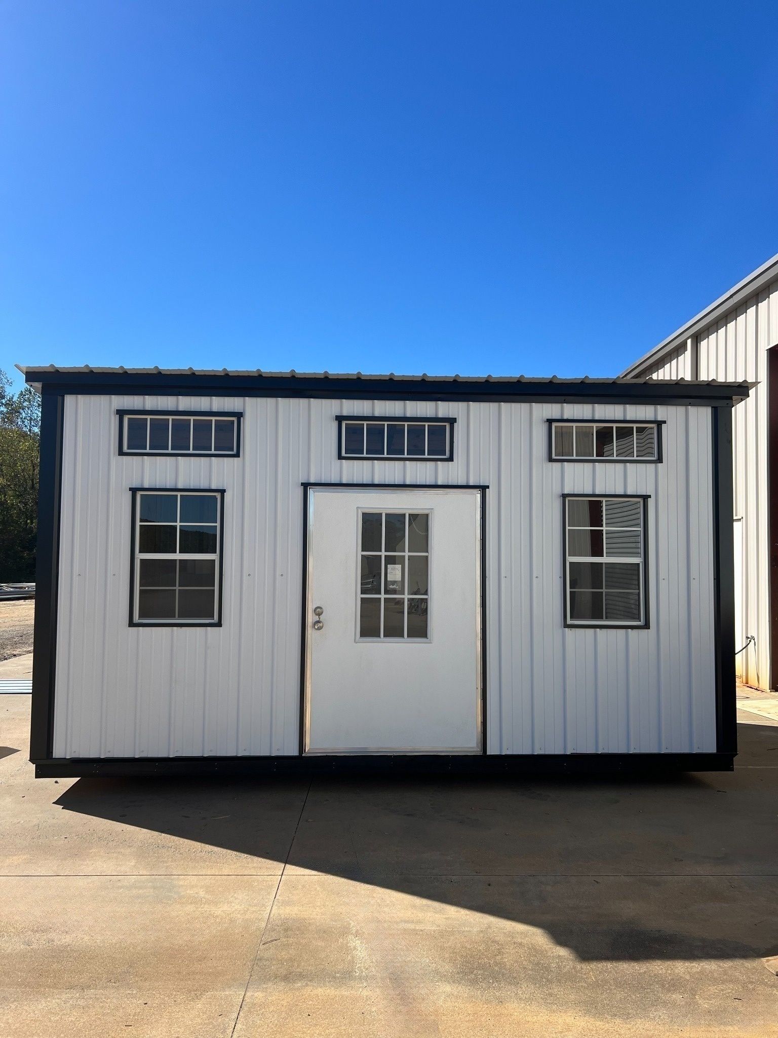White tiny home with black trim, windows, and door against a blue sky.