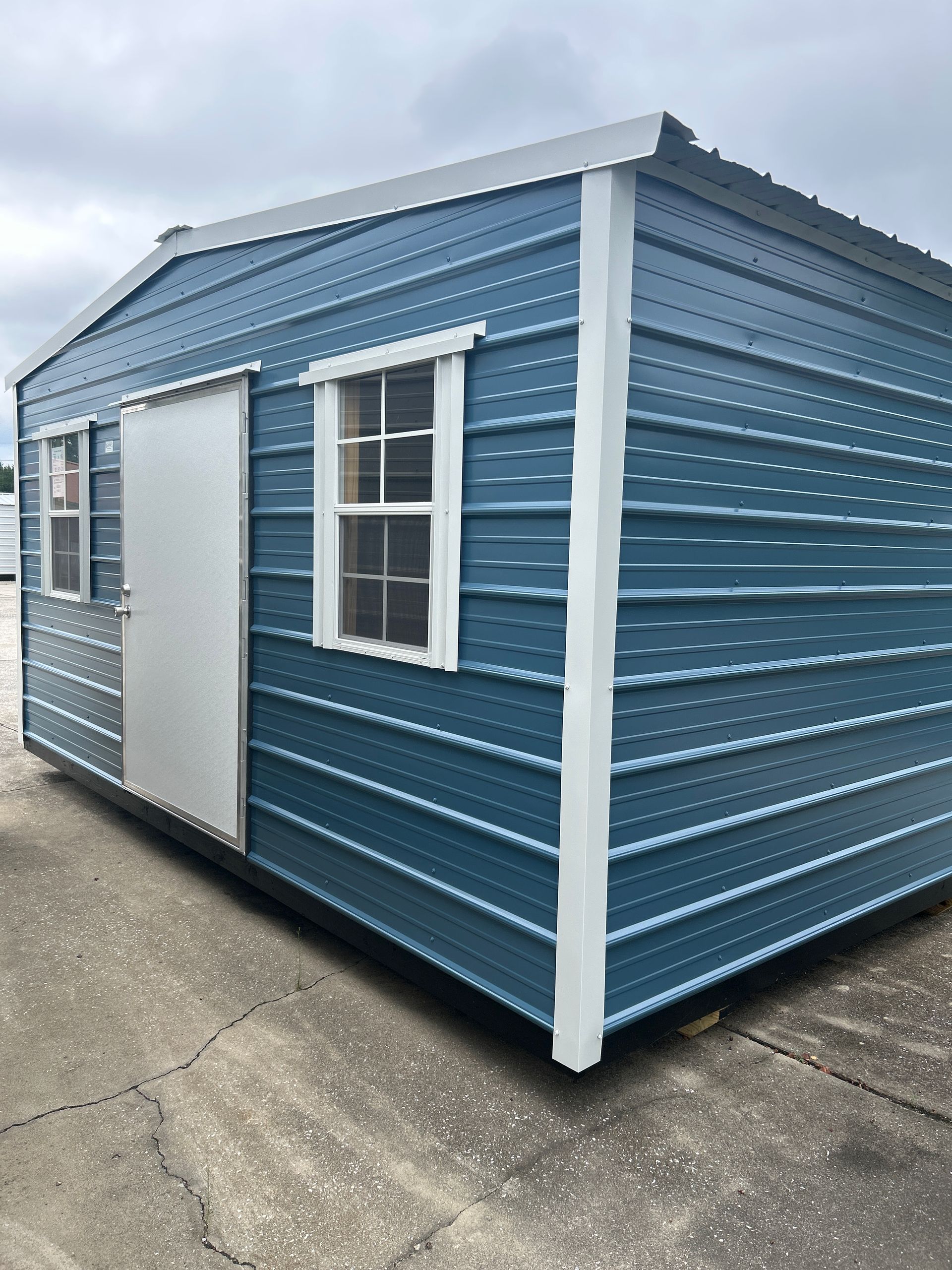 Blue metal storage shed with white trim and windows.