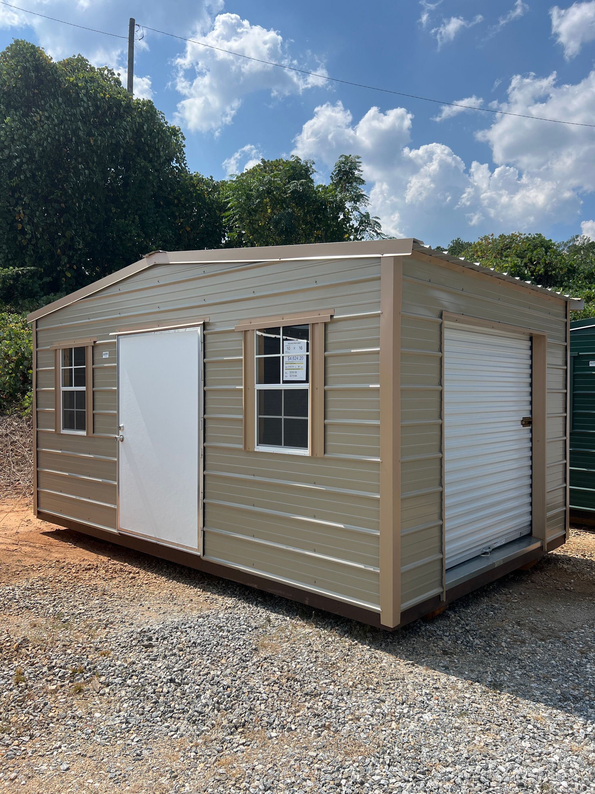 Tan shed with brown trim, SOLD sign on the door, windows, and overcast sky.