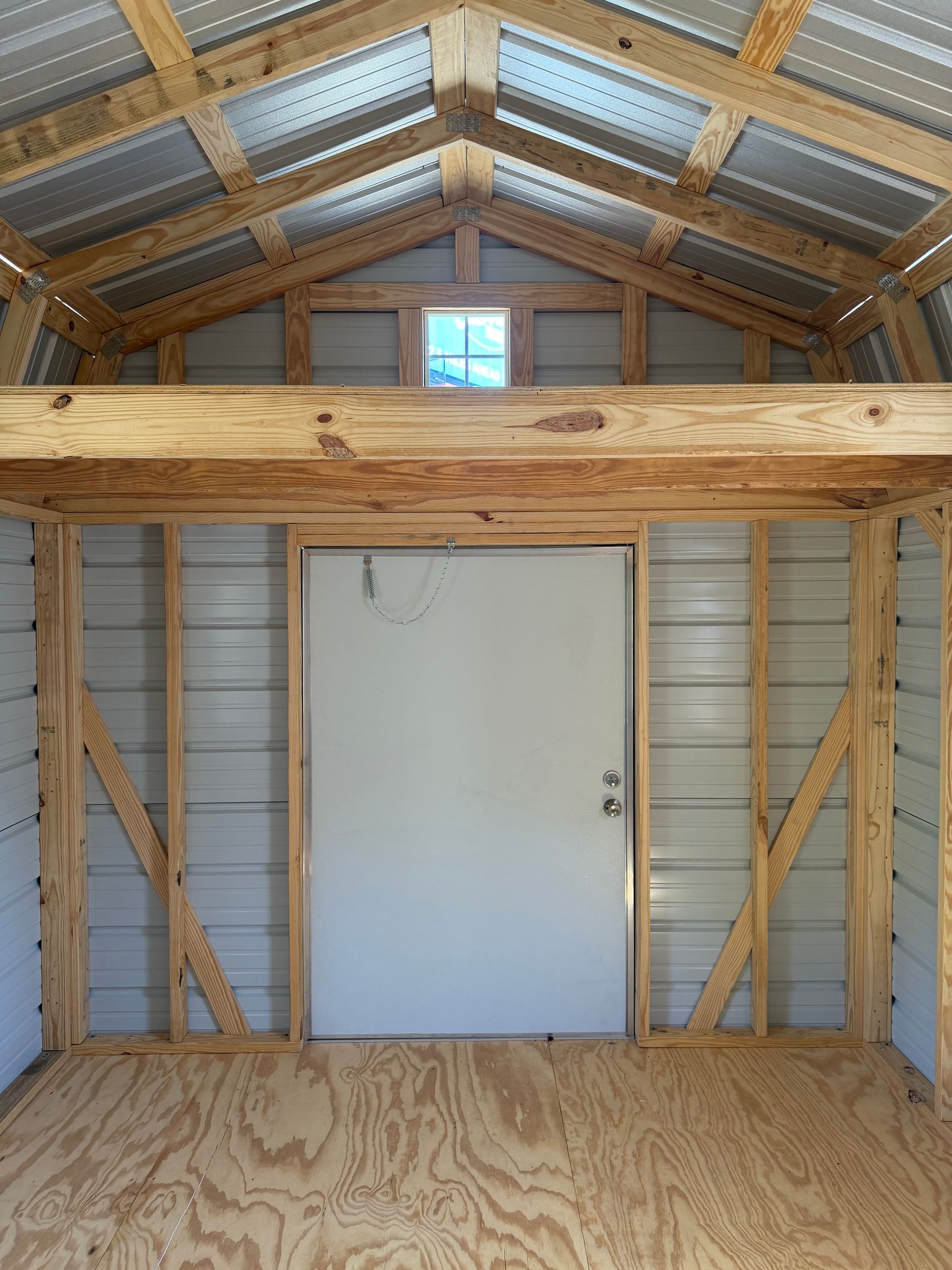 Interior of a wooden shed with plywood floor, white door, and loft storage space overhead