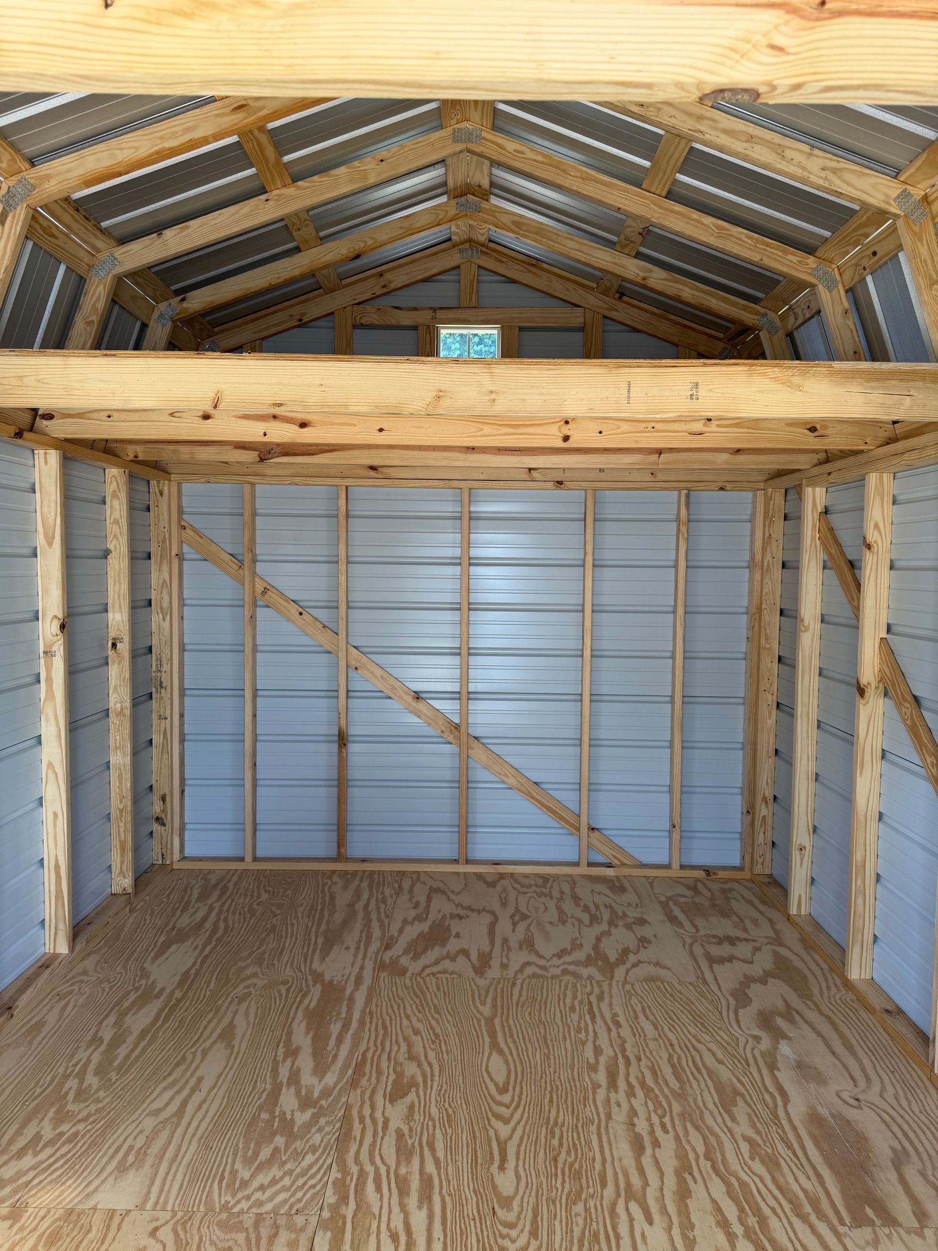Interior of a small wooden shed with exposed framing, plywood floor, and metal roof panels