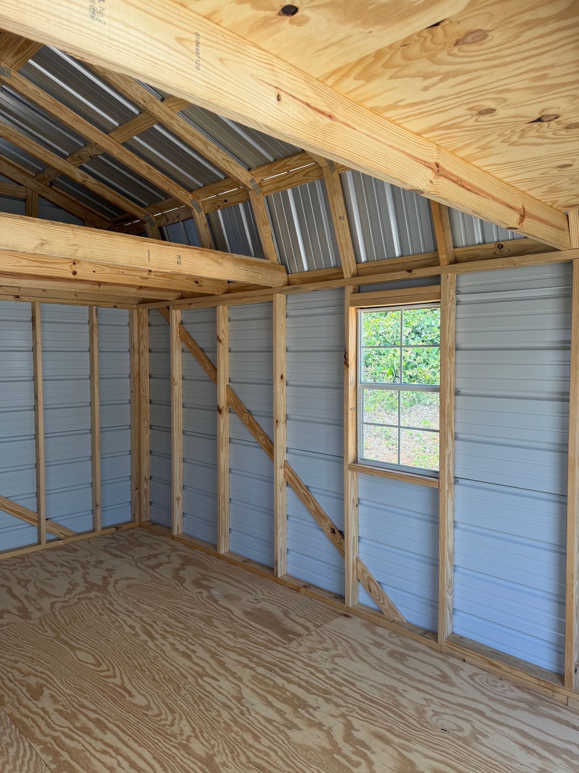 Interior of unfinished shed with exposed wood framing, blue painted walls, and a small window.