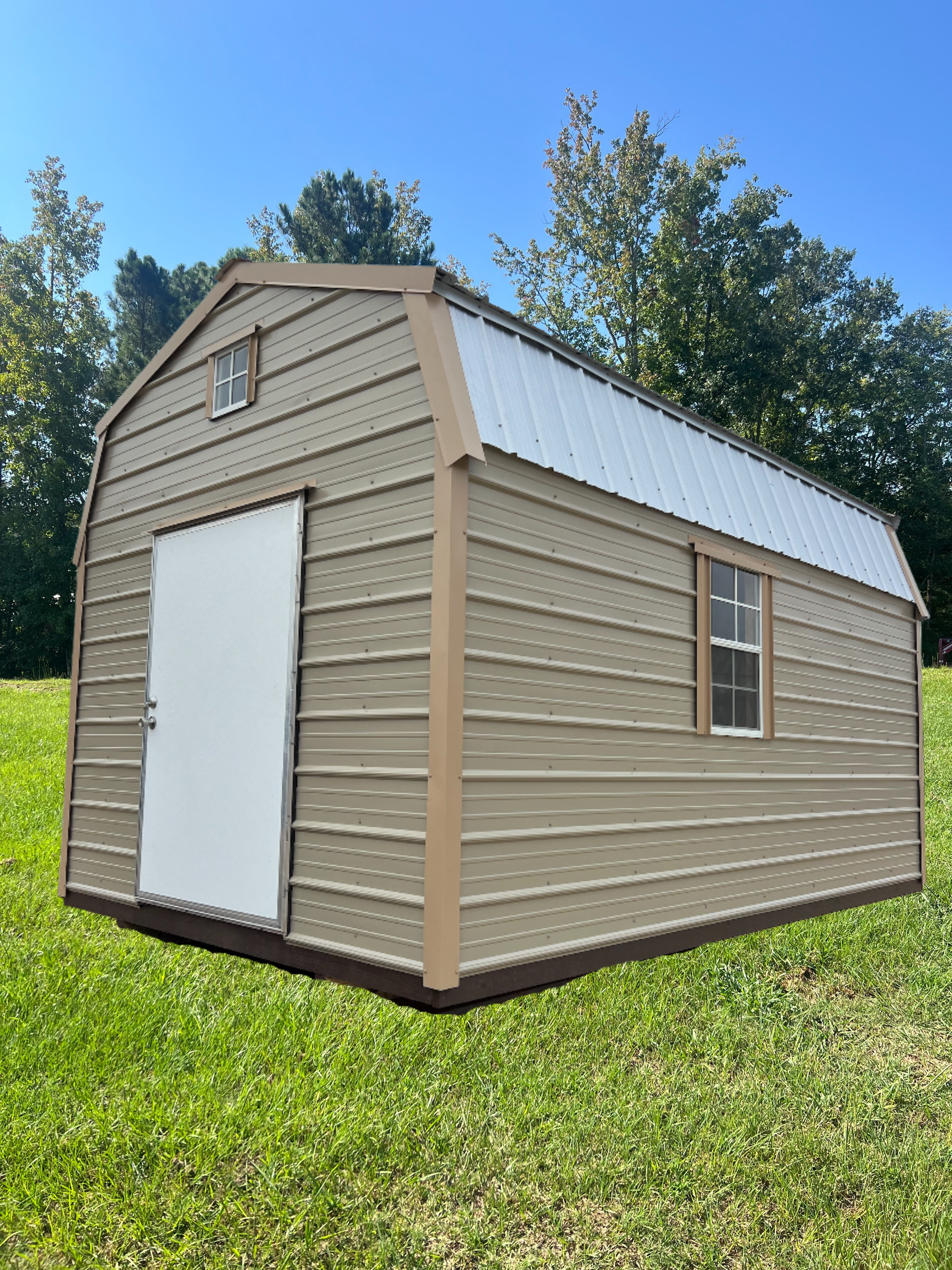 Tan barn-shaped shed with white door, window, and metal roof on green grass against blue sky.