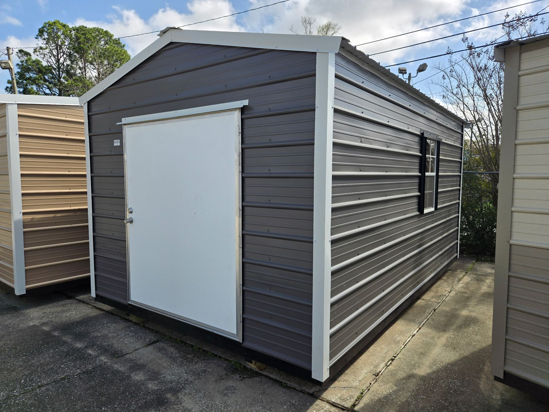 Gray storage shed with white door, window, and trim, on a concrete surface.