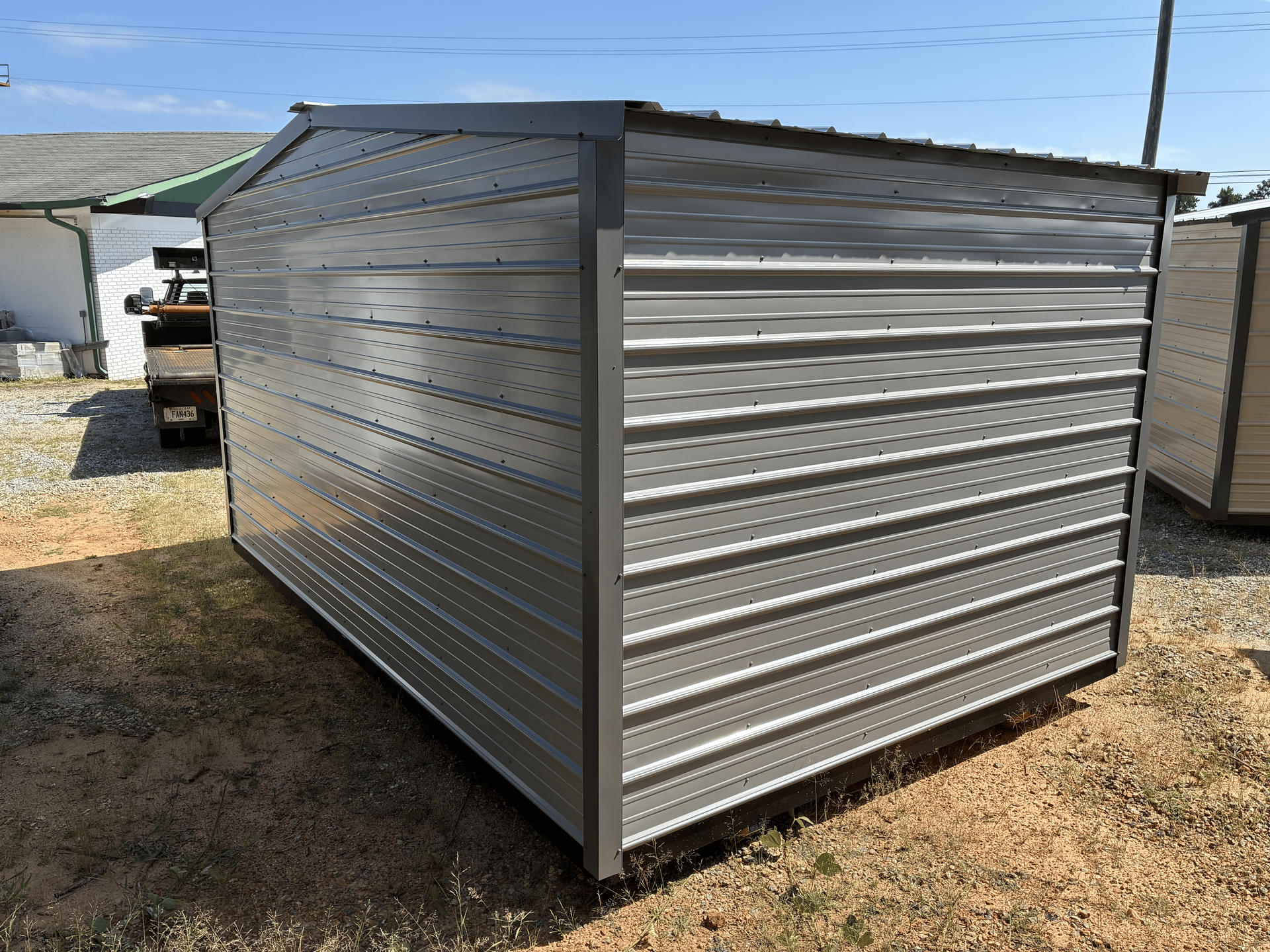 Gray metal storage shed with corrugated sides on a gravel lot under a clear sky
