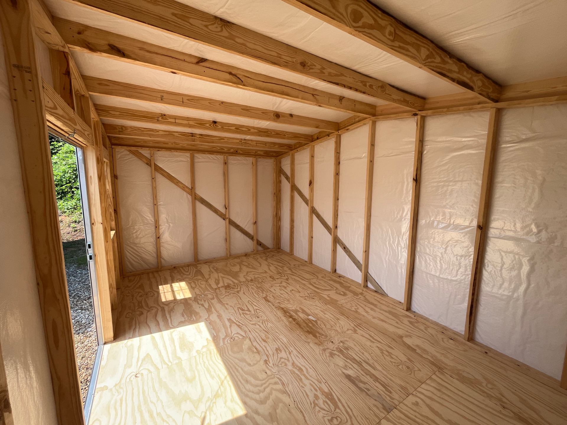 Partially finished shed interior with exposed wood framing, plywood floor, and insulated walls in daylight