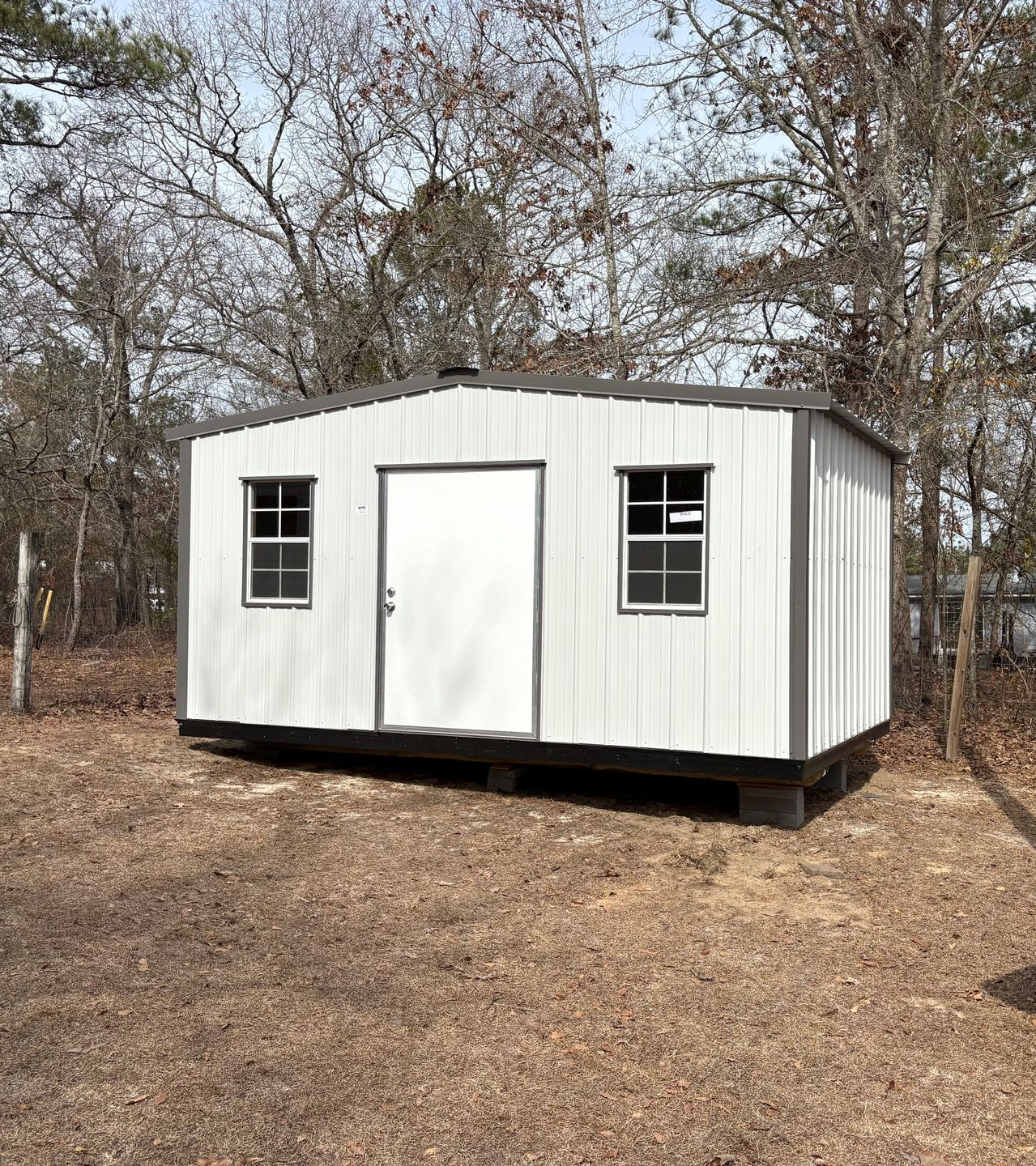 Light gray shed with white door and windows, in a yard with trees.