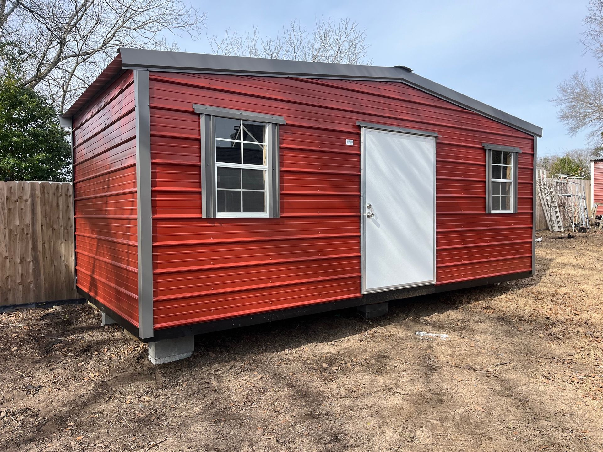 Red shed with a white door and two windows.