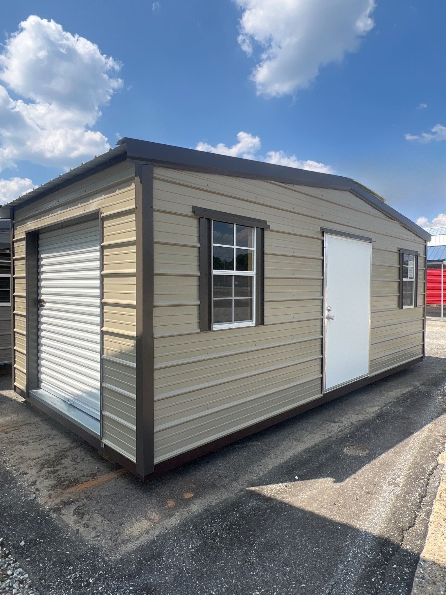 Tan metal shed with brown trim; roll-up door, window, and door; blue sky background.