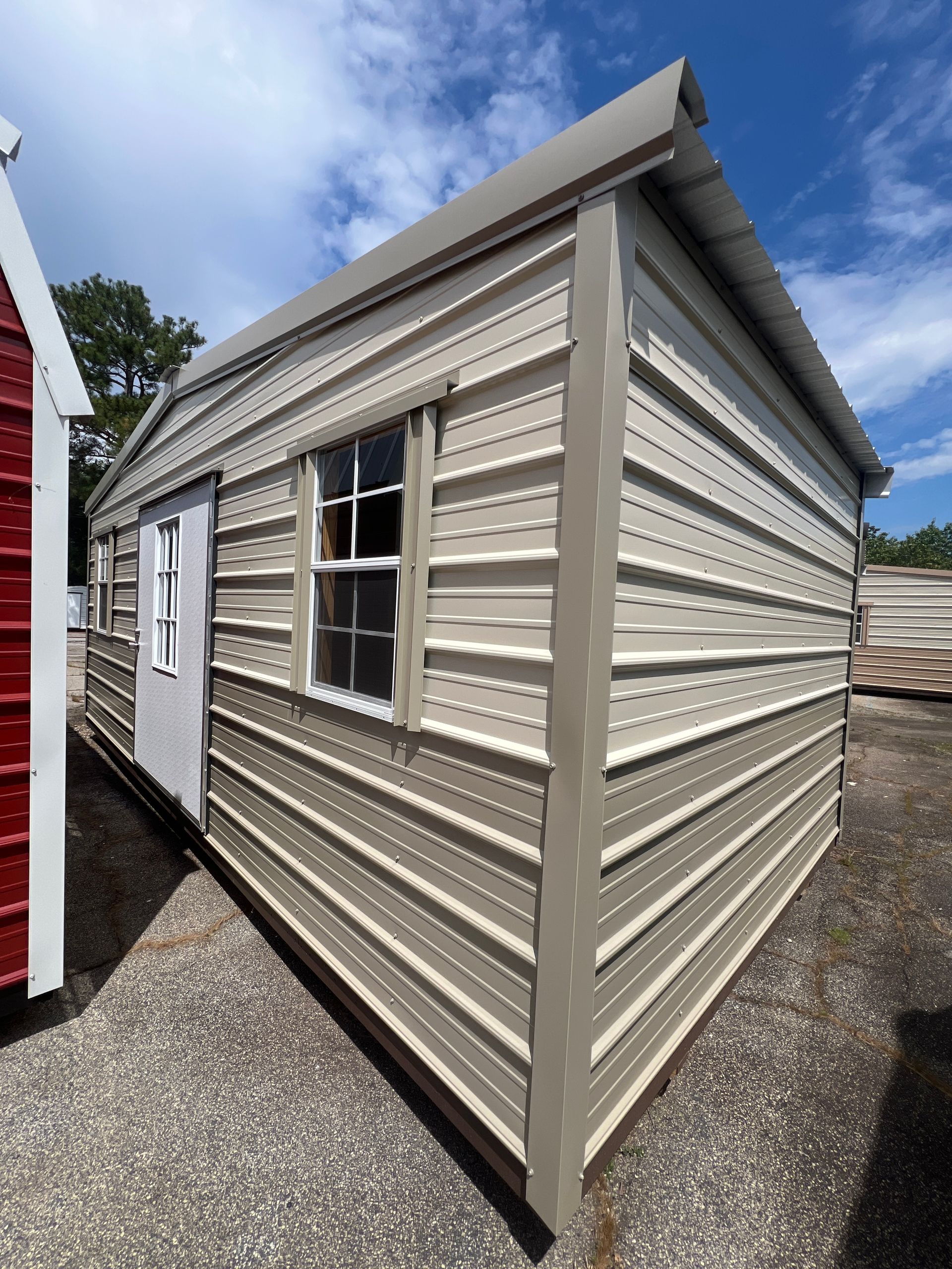 Tan metal shed with white door and window on a sunny day.