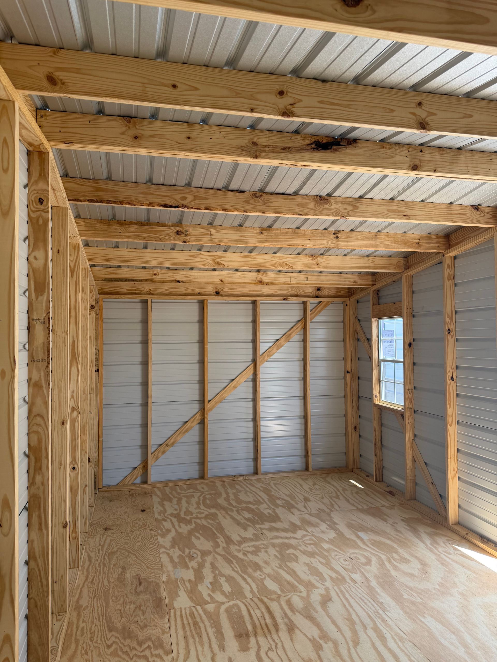 Empty unfinished wooden interior with exposed beams, plywood floor, and corrugated metal wall panels