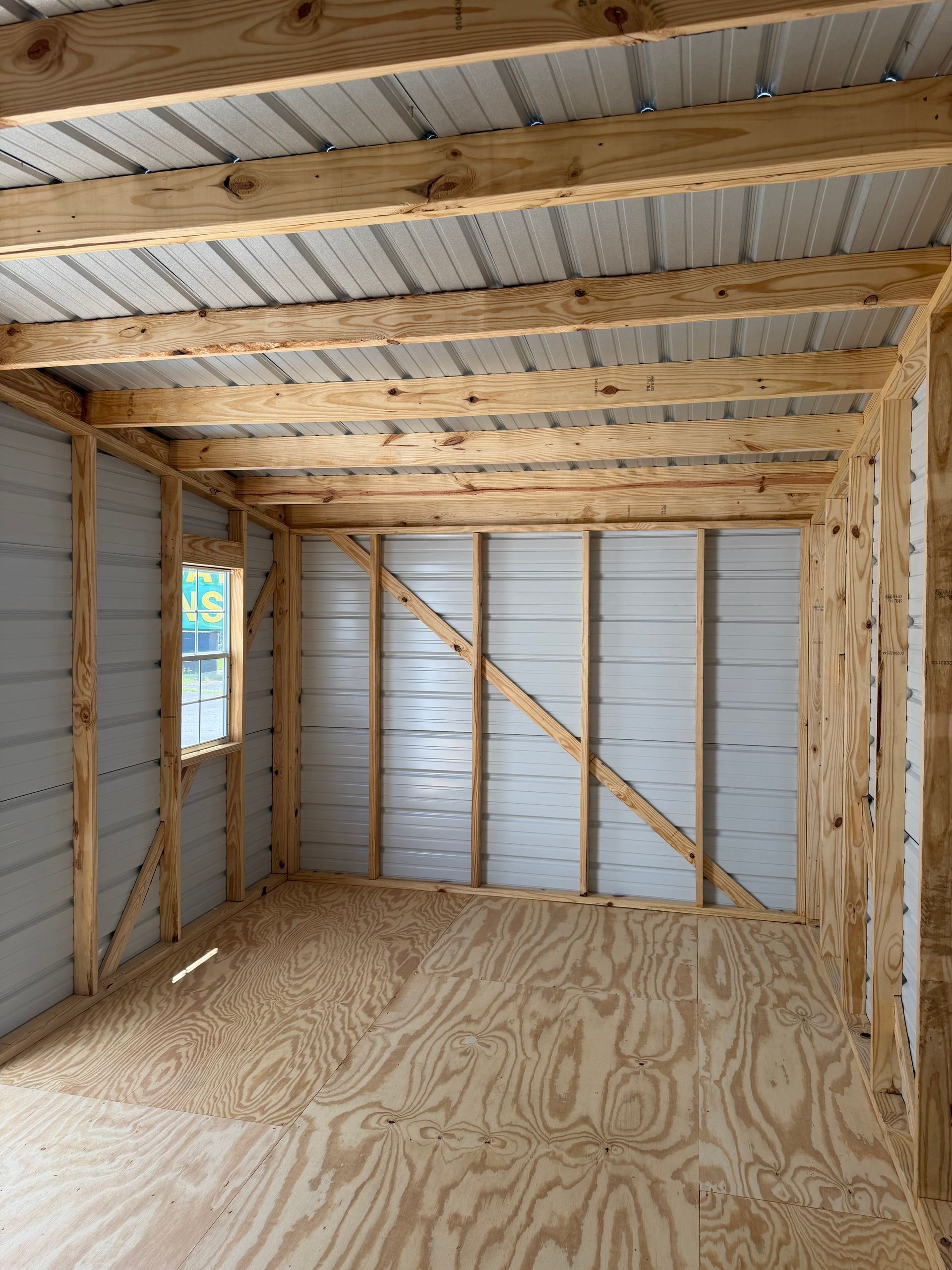 Interior of a small unfinished shed with plywood floor, exposed wood framing, and corrugated metal walls and roof.