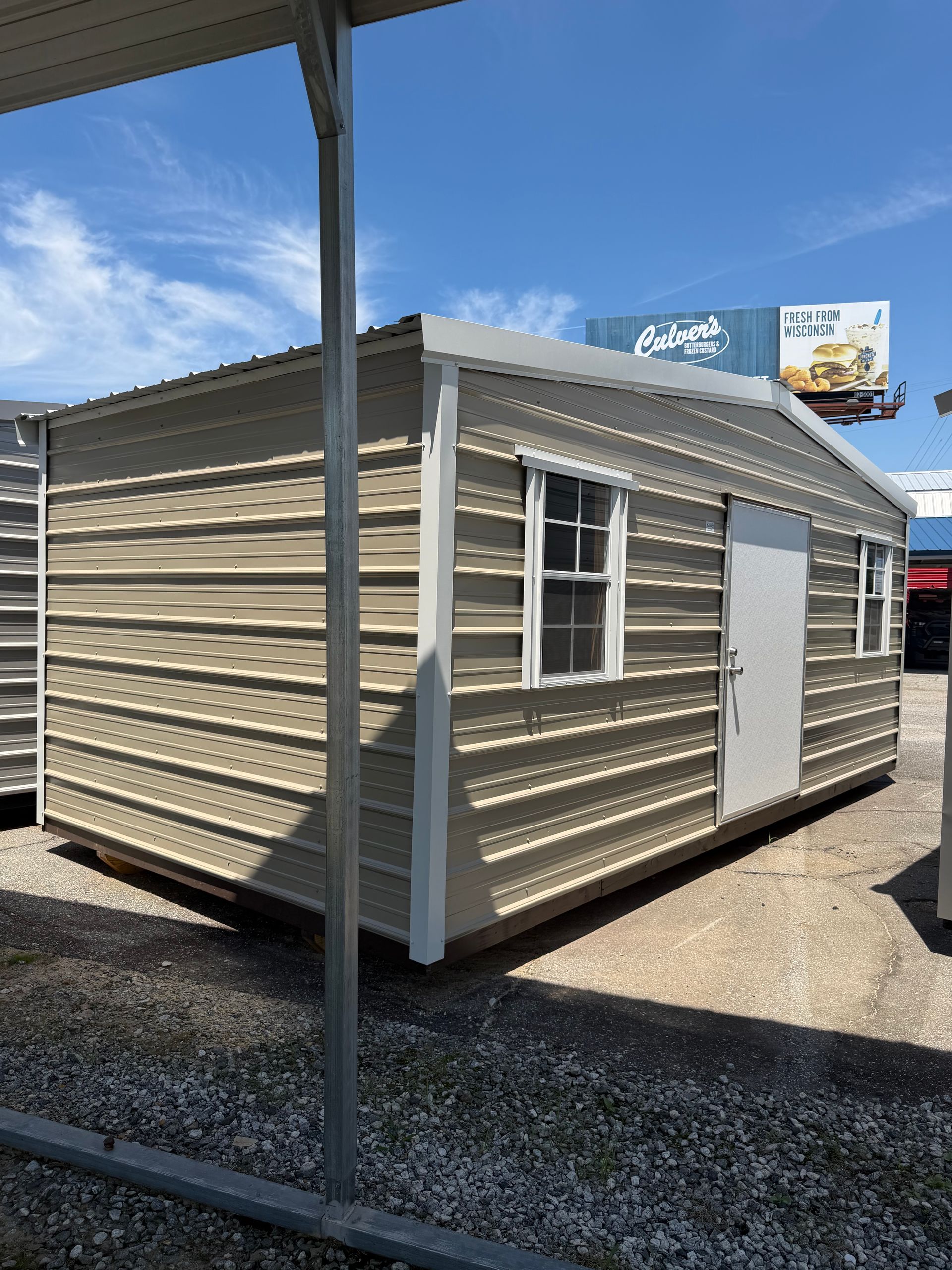 Small beige modular building with white trim and a door, shown outdoors on gravel under a blue sky.