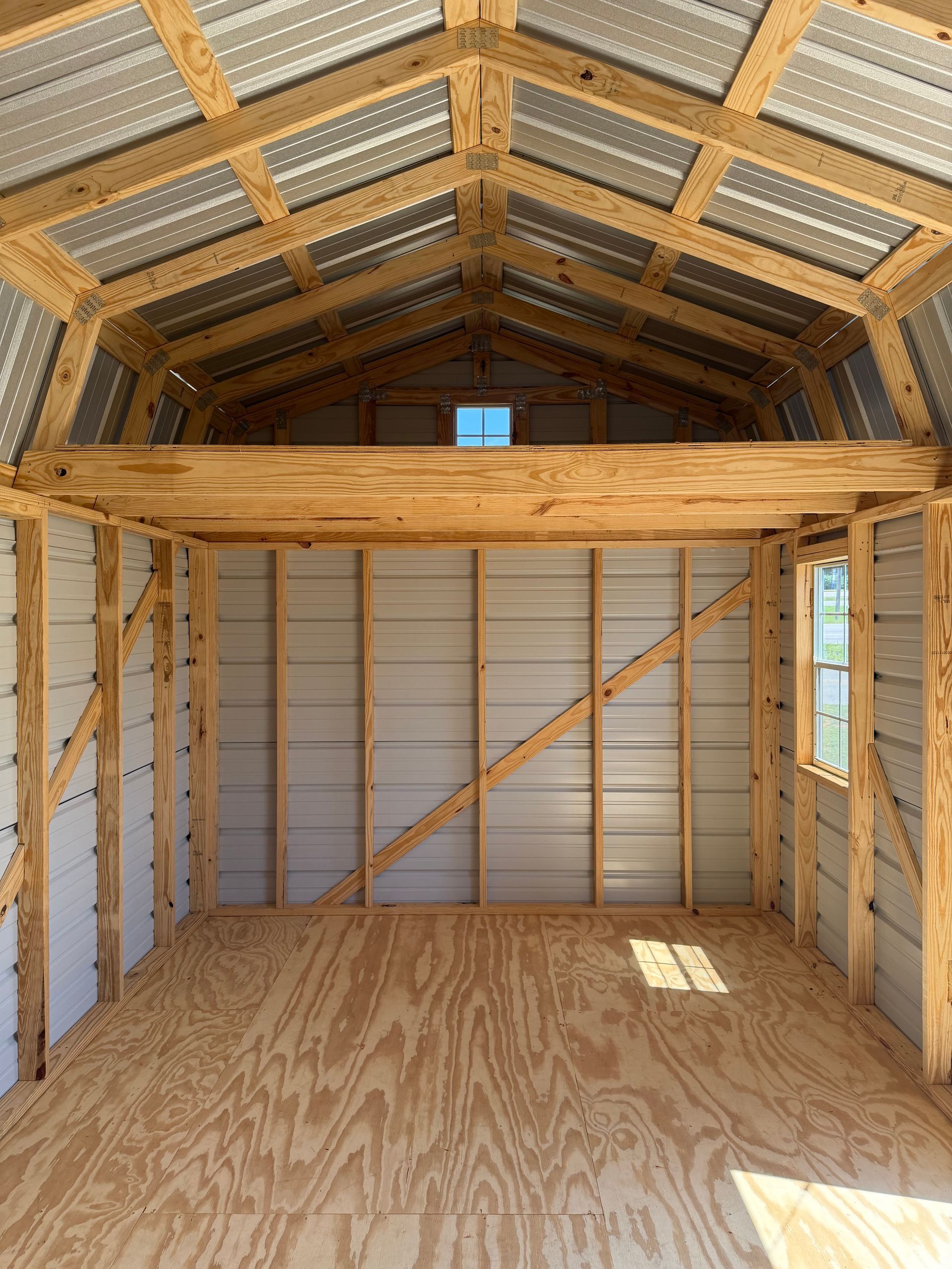 Interior of an unfinished wooden shed with plywood floor, framed walls, and a loft area.