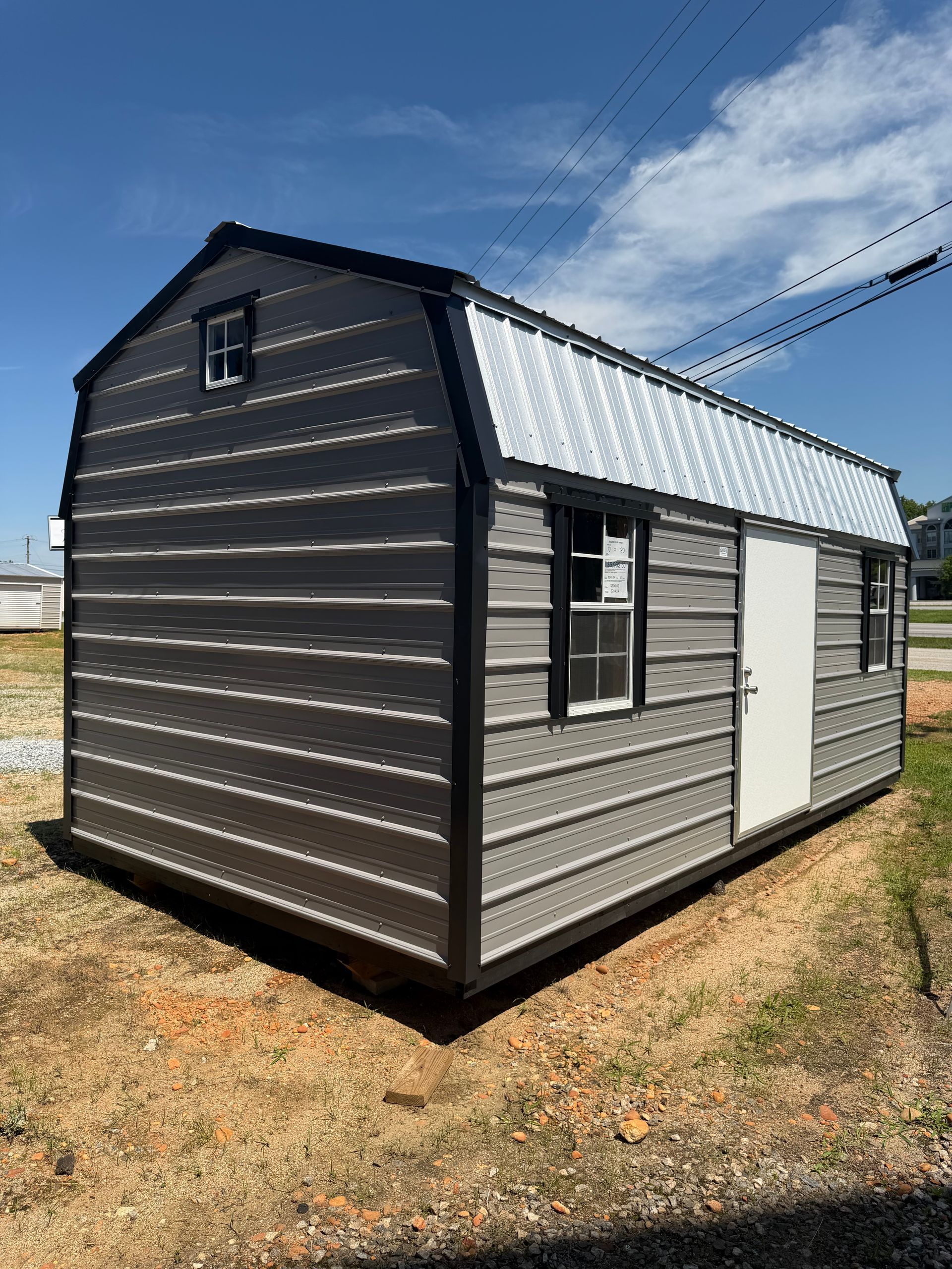 Small gray metal shed with white roof panels on dry grass under a blue sky