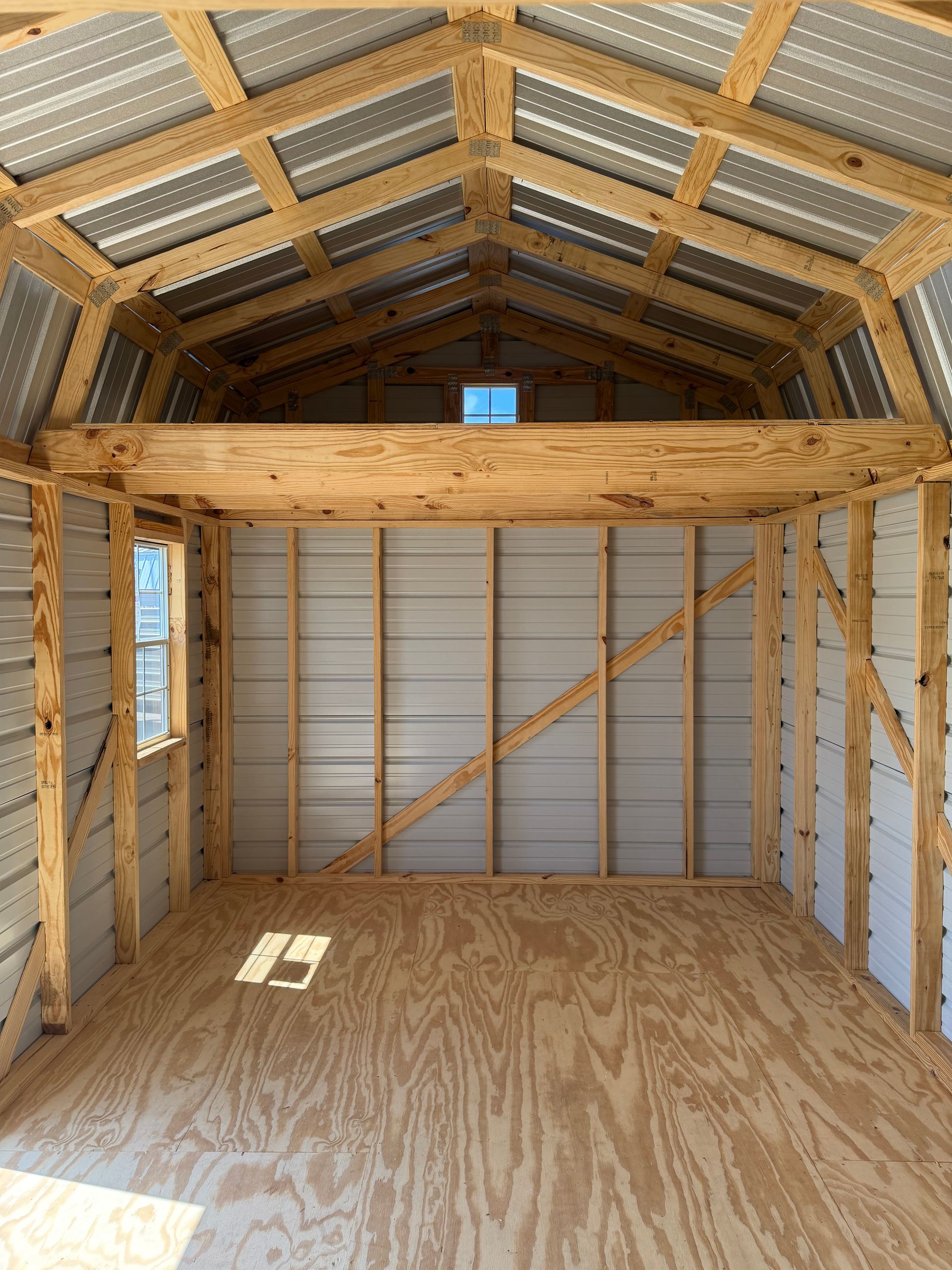 Interior of an unfinished wooden shed with plywood floor, rafters, and exposed insulation.