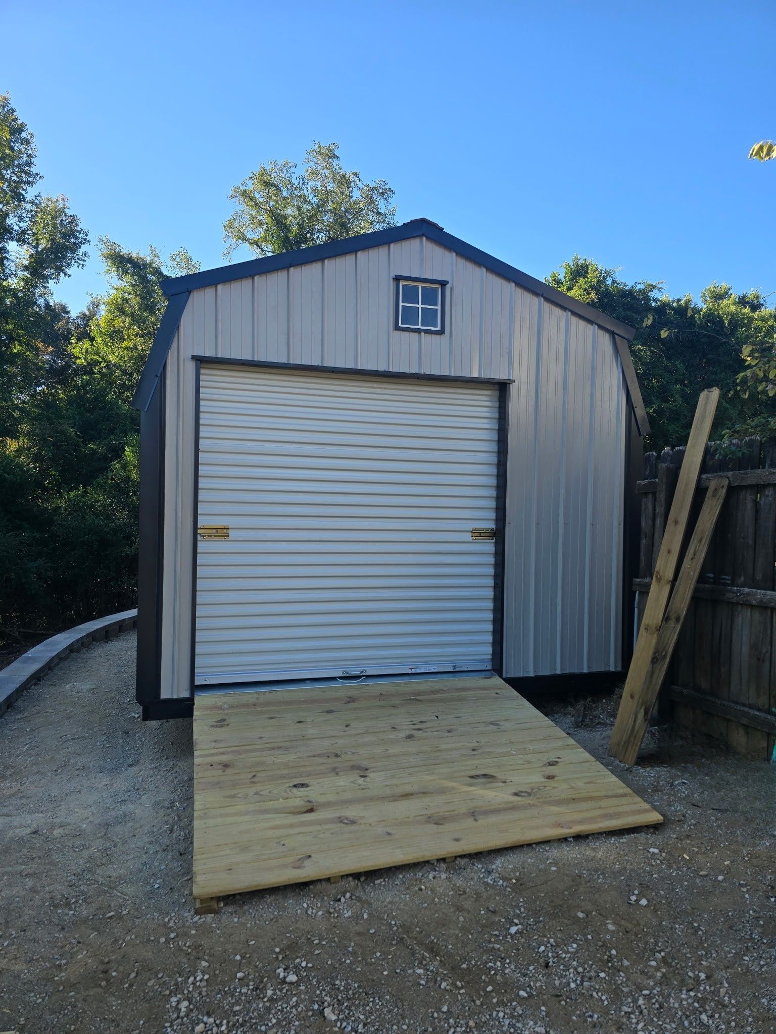Metal shed with a roll-up door, ramp, and small window under a blue sky.