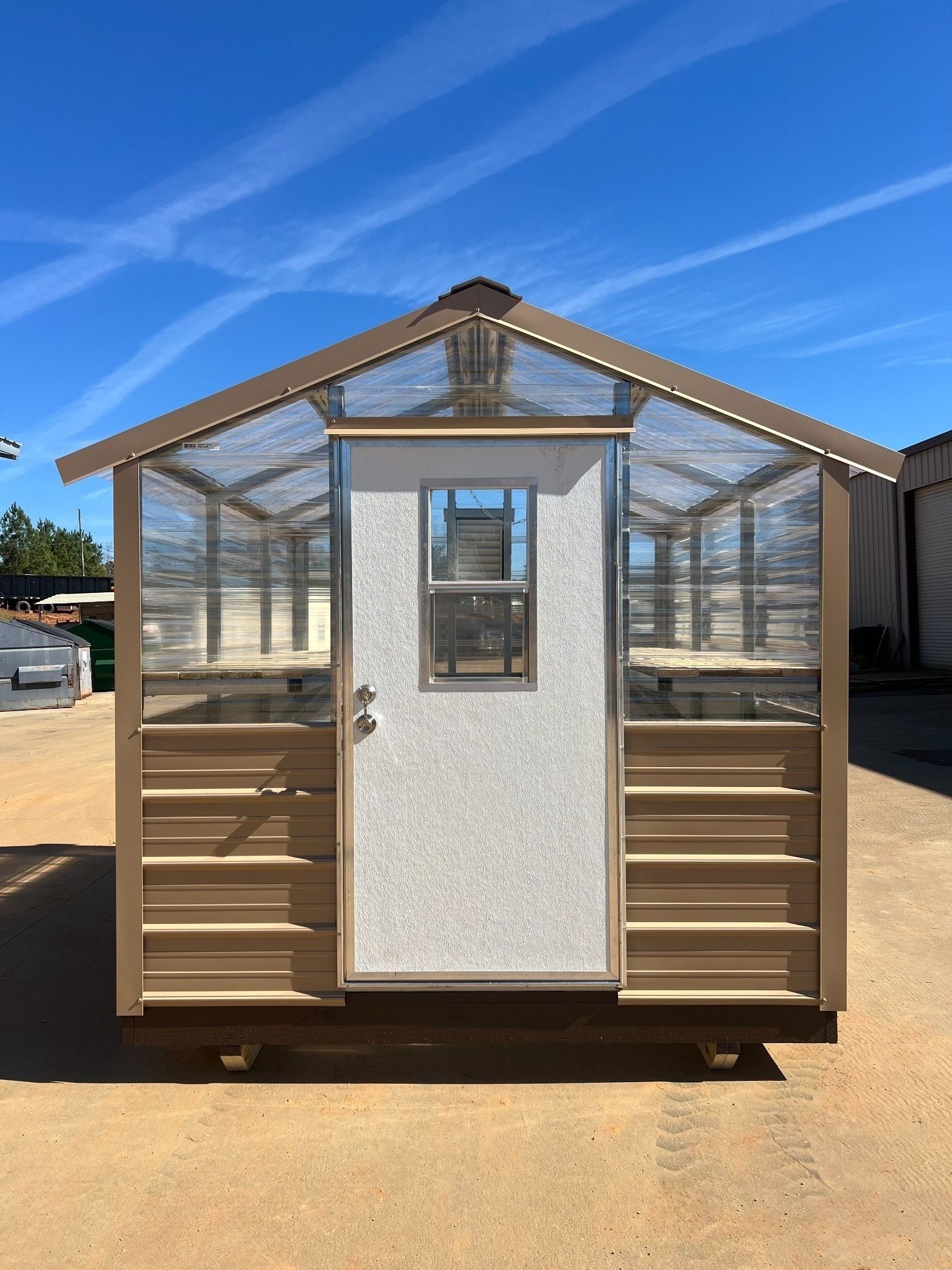 Brown and clear-walled greenhouse with a central door, under a blue sky.