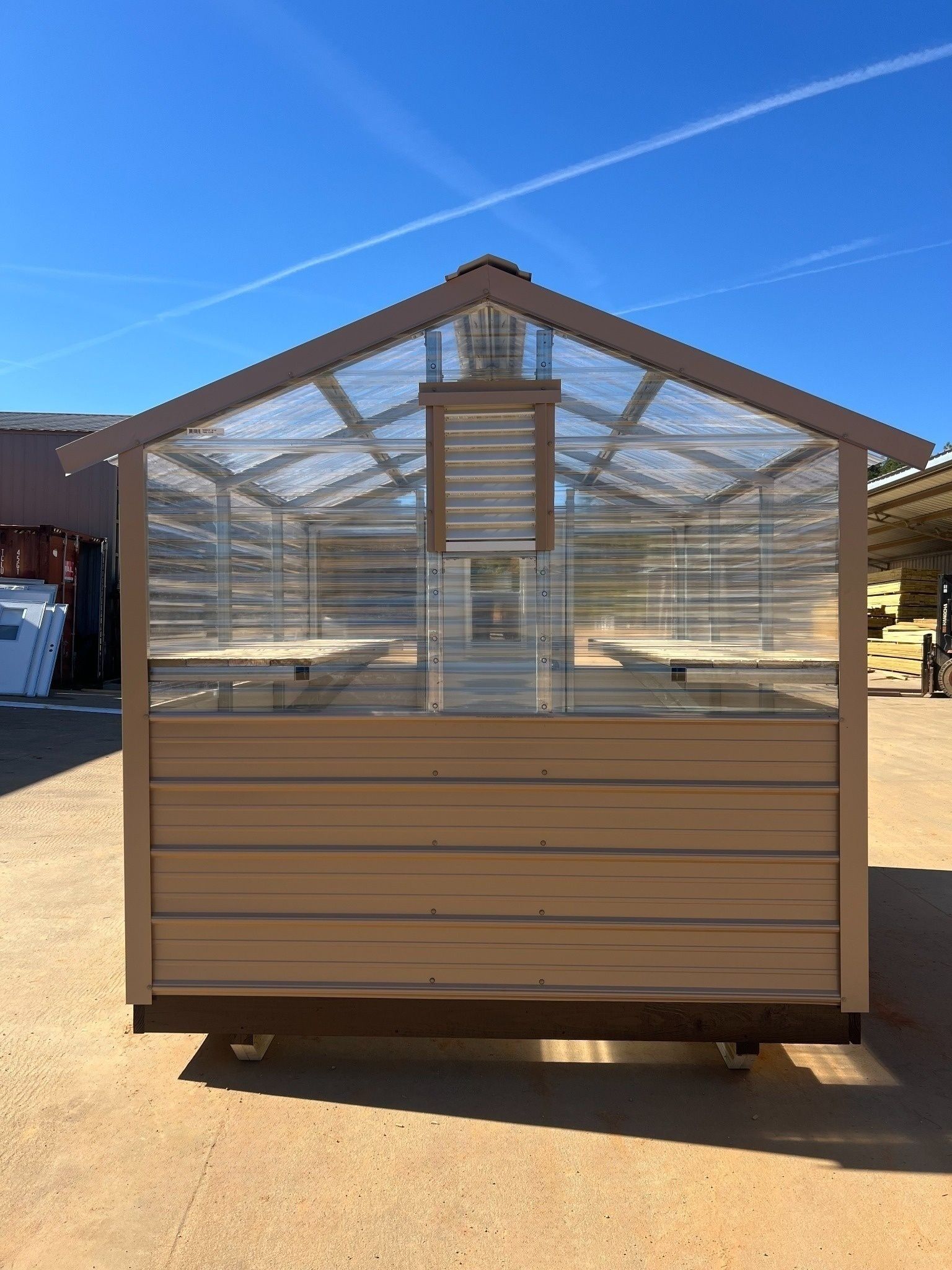 Brown and clear greenhouse with a slanted roof, sitting outside on a sunny day.