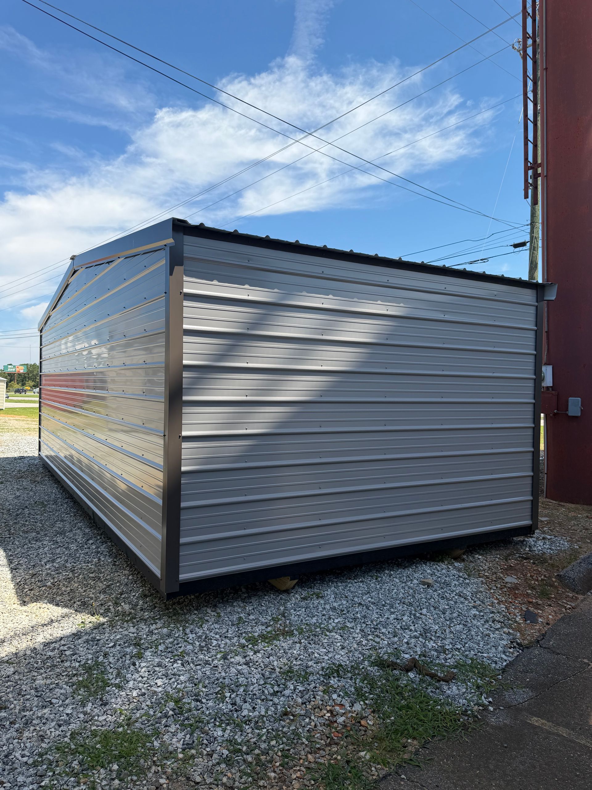 Large silver metal storage container beside a red building on gravel under a blue sky