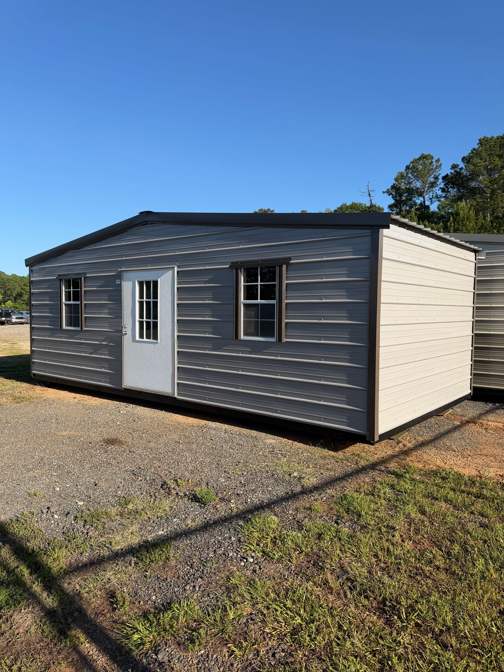 Small gray modular building with white trim on gravel under a clear blue sky.