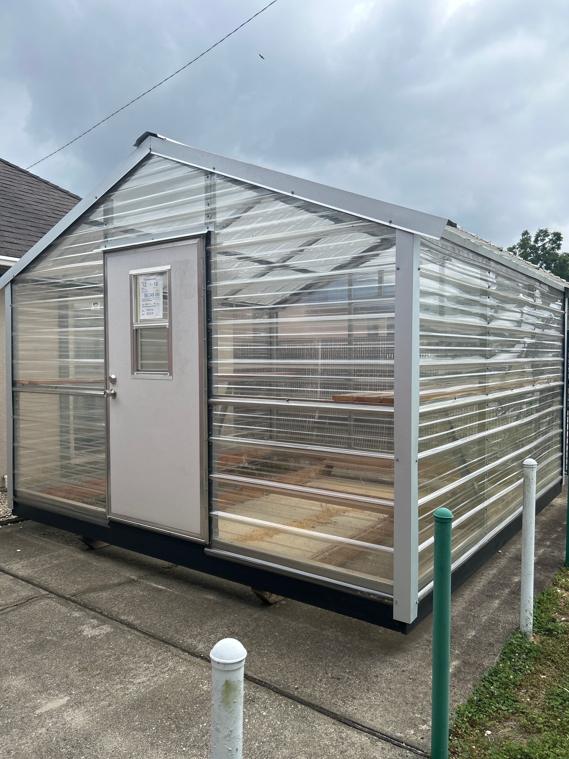 Greenhouse with clear corrugated plastic walls, white frame, and a door, set on a concrete pad.