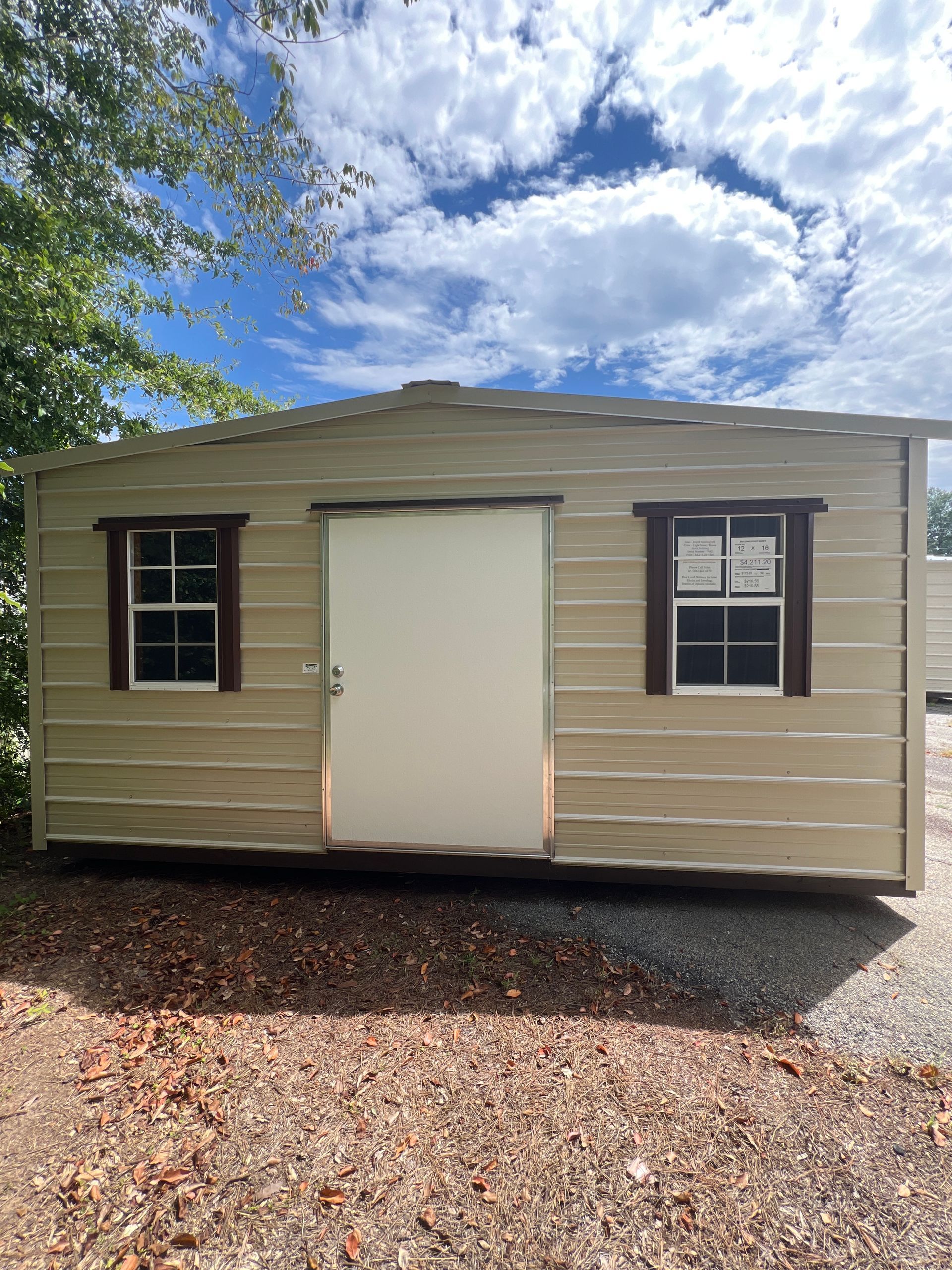 Tan shed with white door and windows, under a blue sky with clouds.