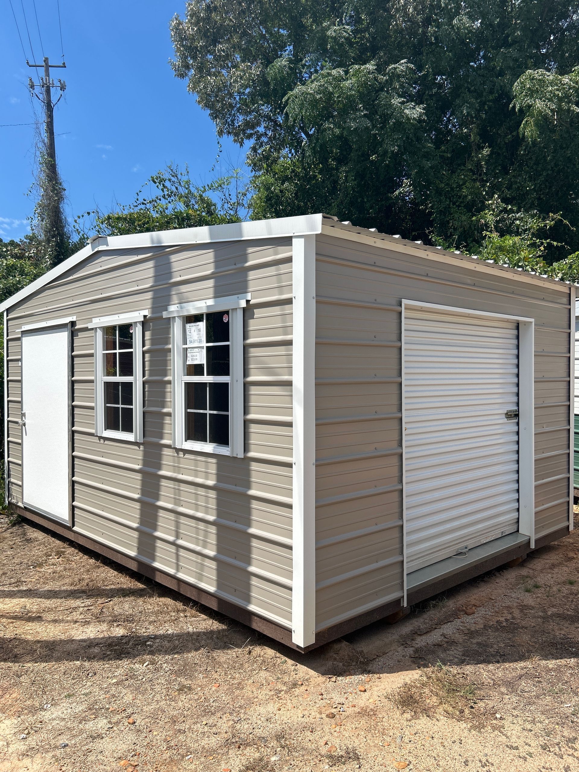 Tan shed with white trim and two windows. A white door is on the left, and a roll-up door on the right.