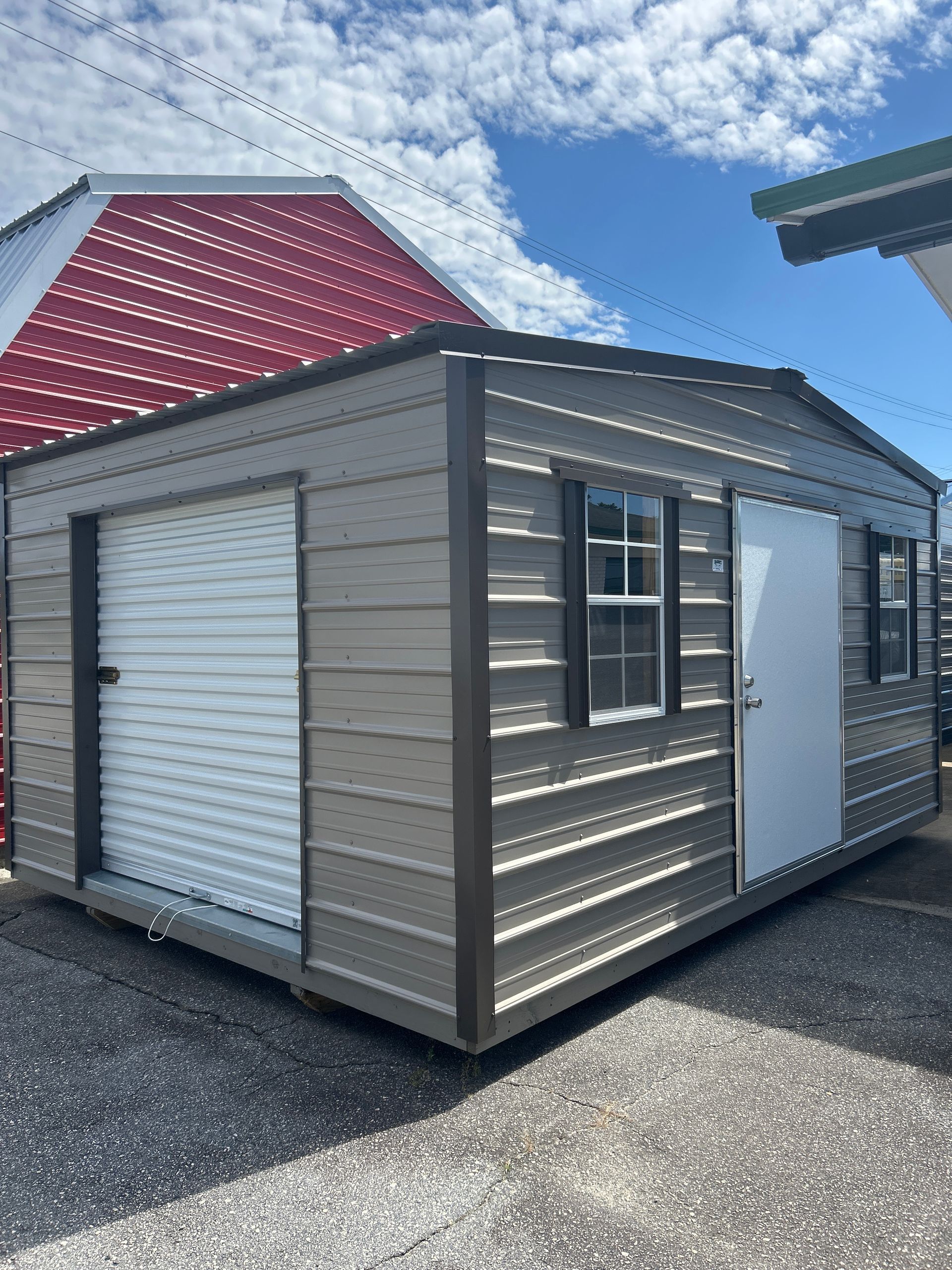 Tan metal shed with a garage door, a window, and a white door, against a blue sky.