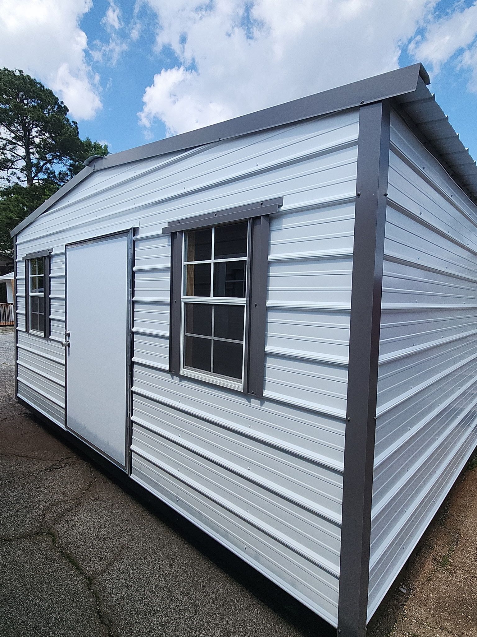 White corrugated metal shed with a window and door, viewed from the side under a cloudy sky