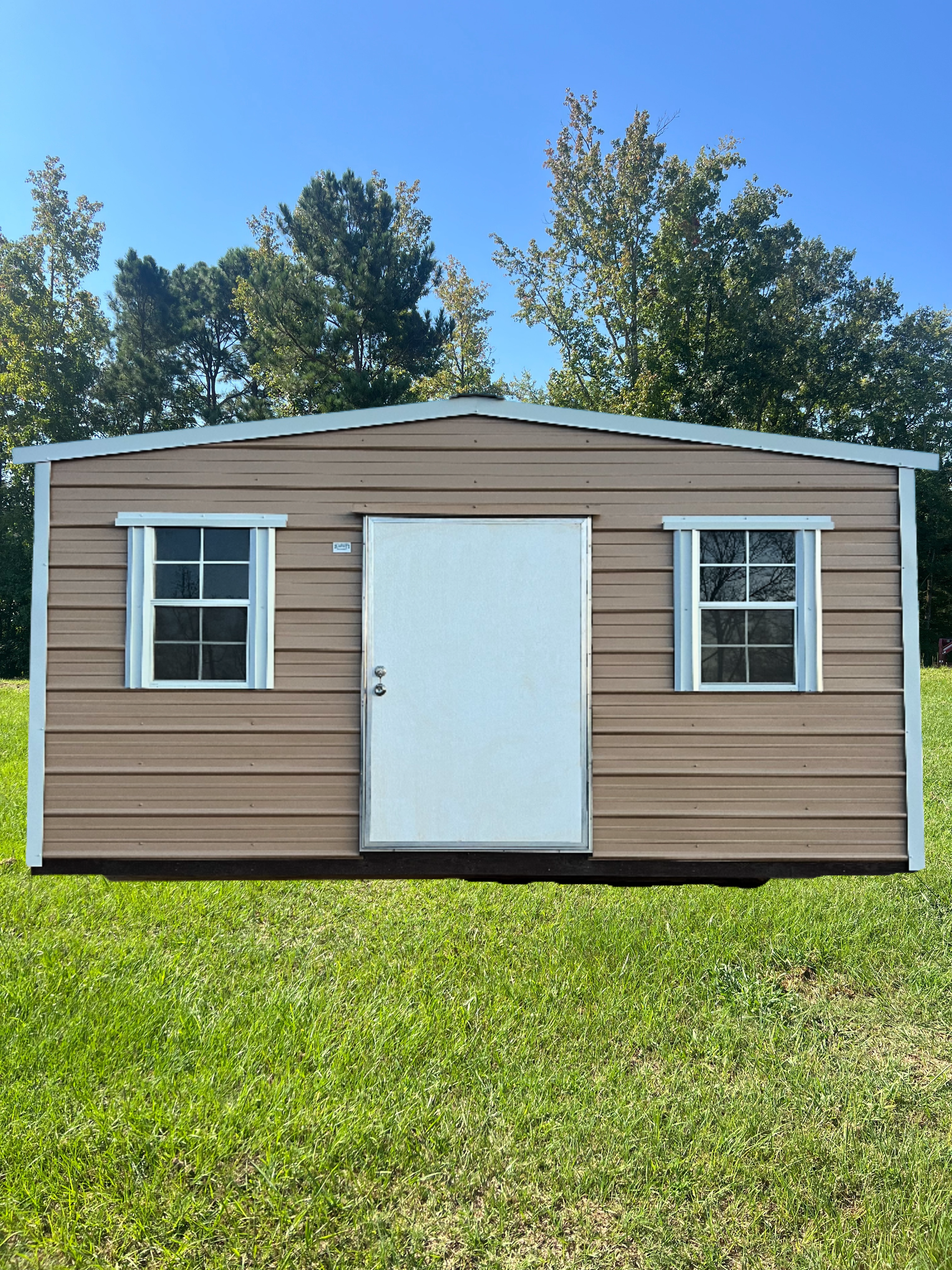 Tan metal shed with white door and windows on a grassy lawn.