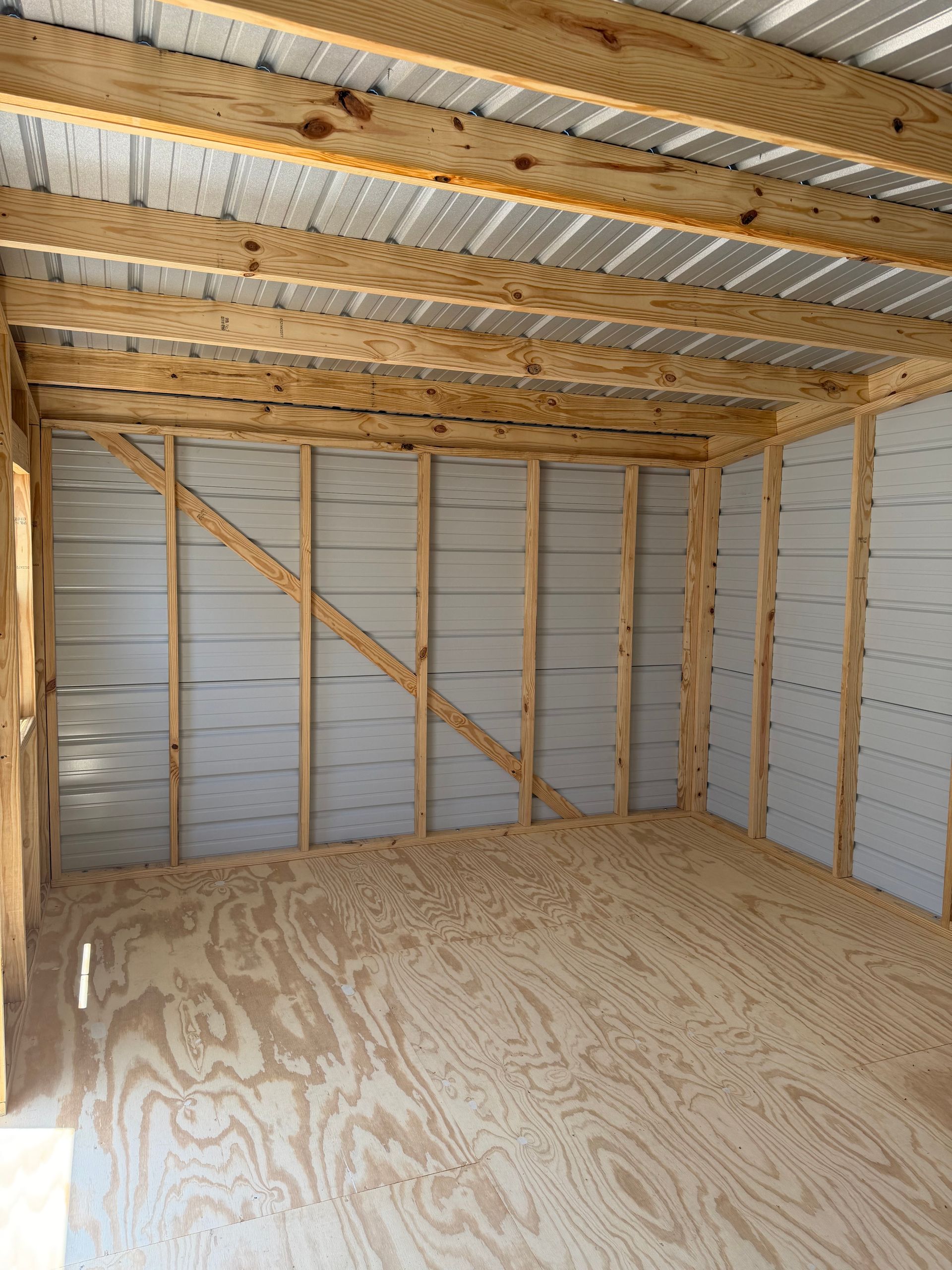 Unfinished wooden shed interior with plywood floor, exposed framing, and corrugated metal roof