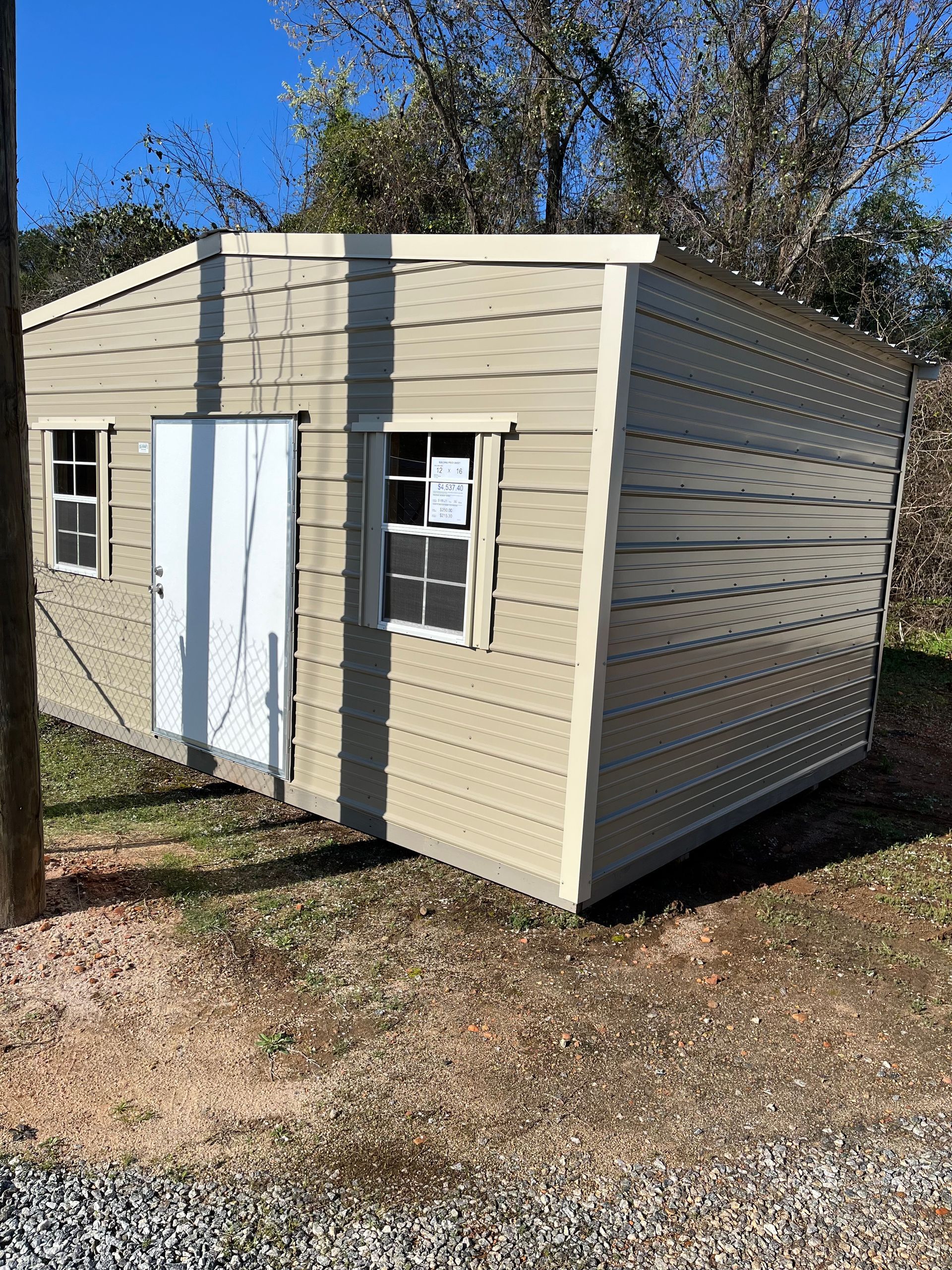 Beige shed with white door and windows; outdoors on grass.