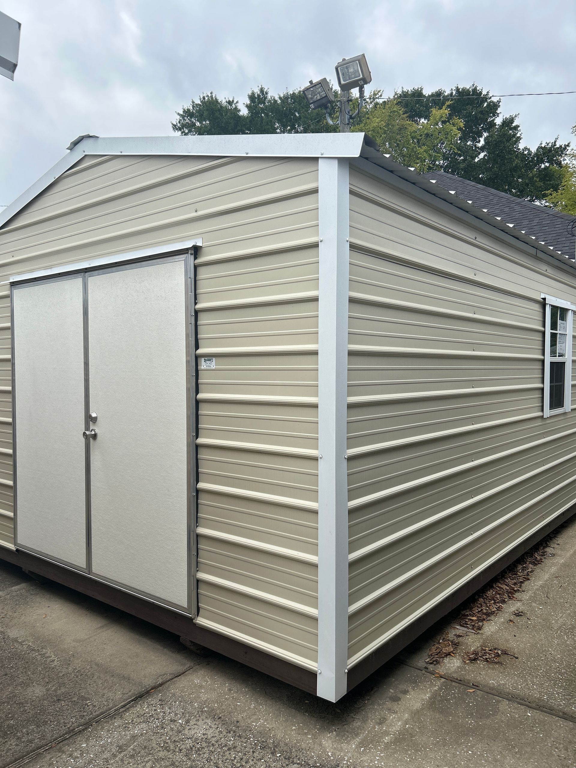 Tan metal shed with double doors and a small window.