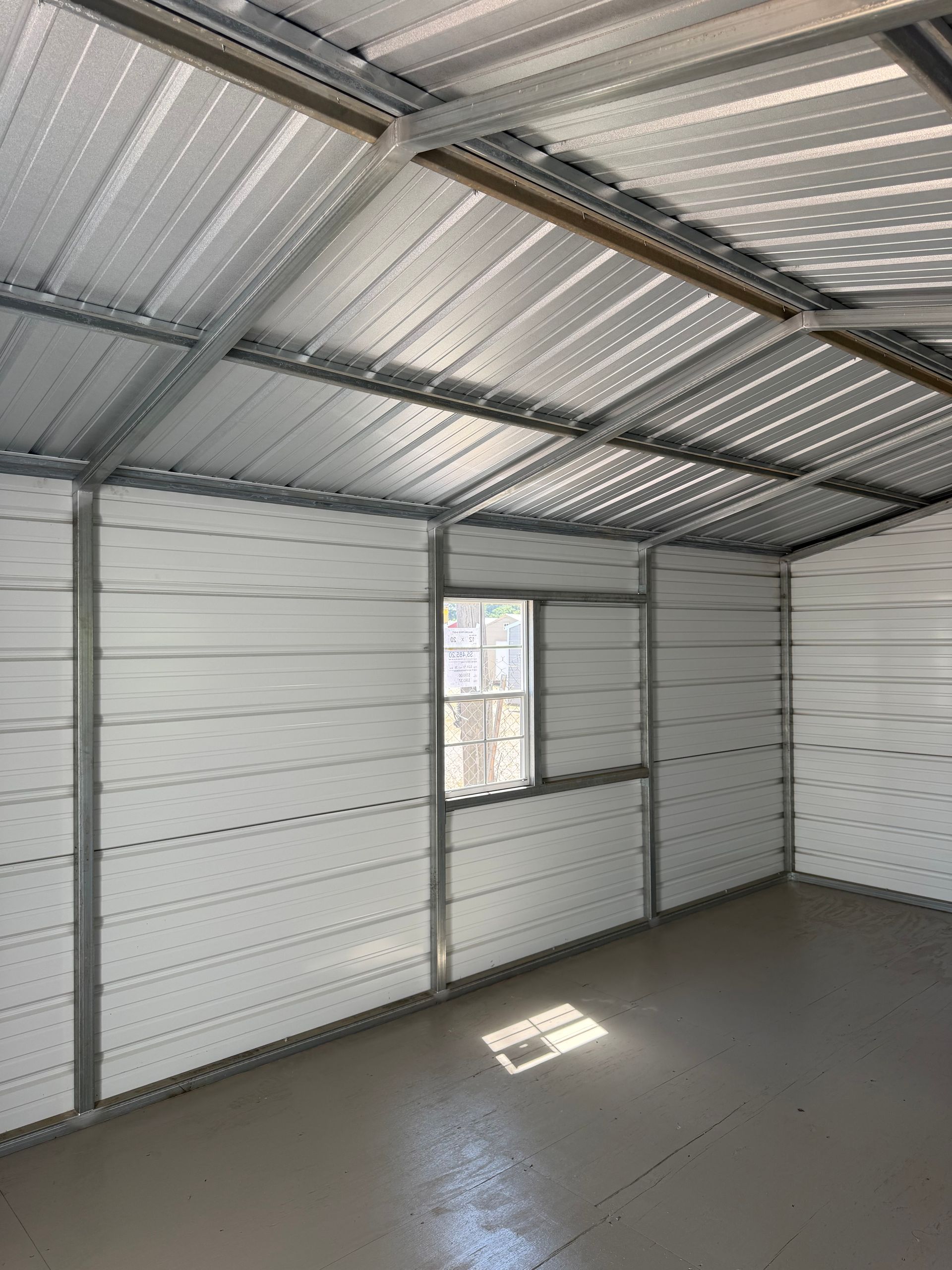 Empty metal-walled room with corrugated roof and a small window, lit by sunlight on the floor