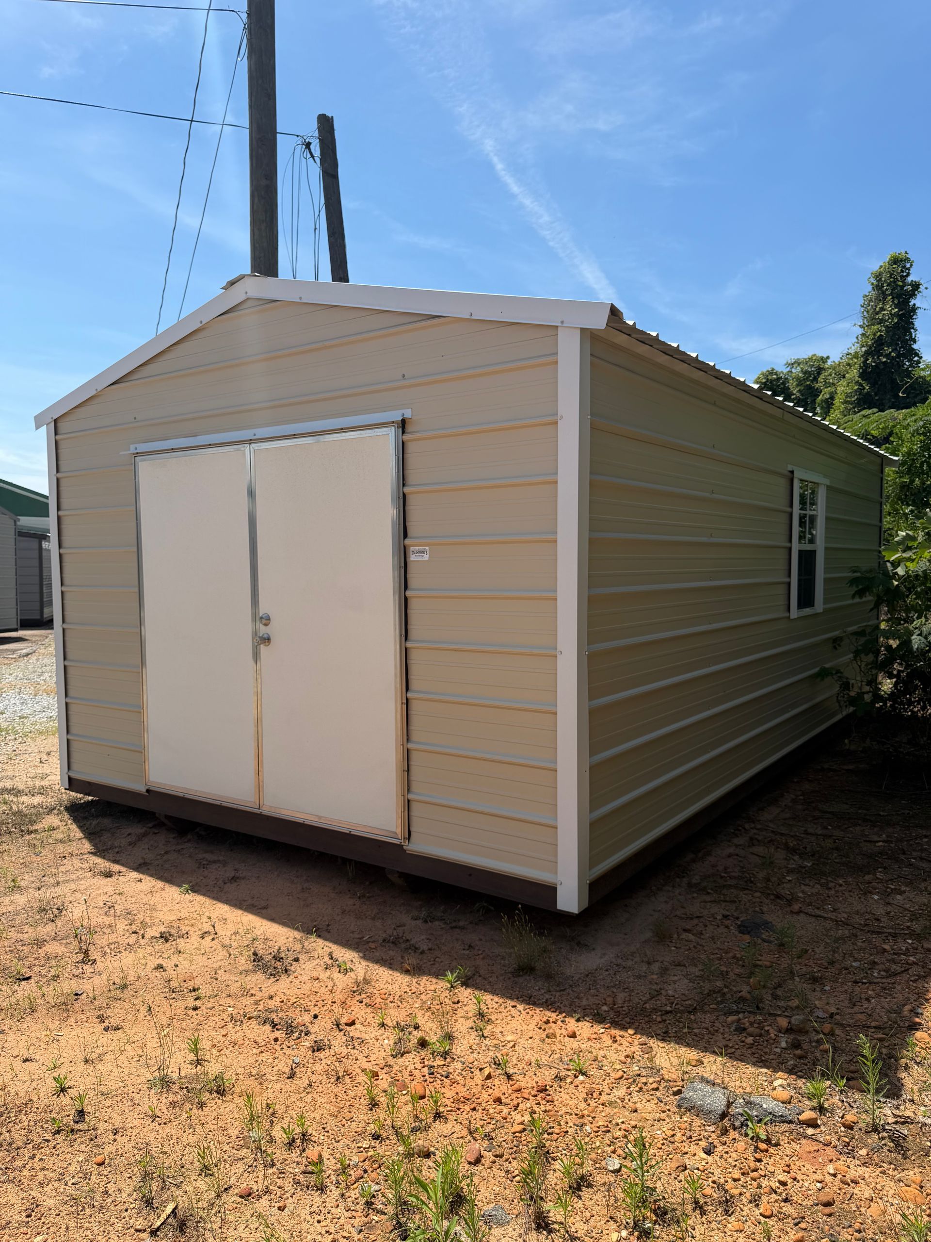 Beige storage shed with double doors, set on gravel under a blue sky