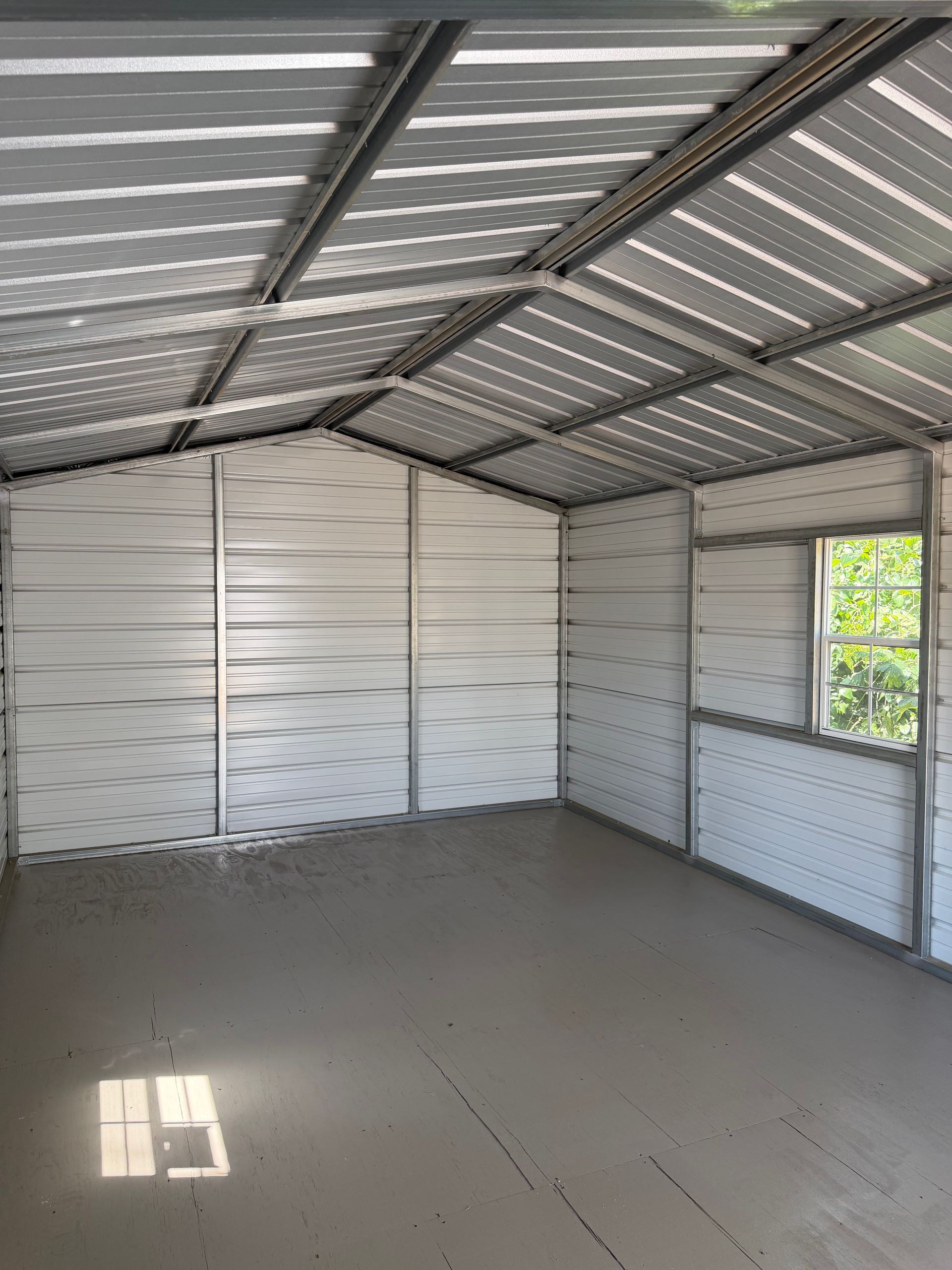 Empty metal shed with corrugated roof, white walls, concrete floor, and a small window letting in daylight