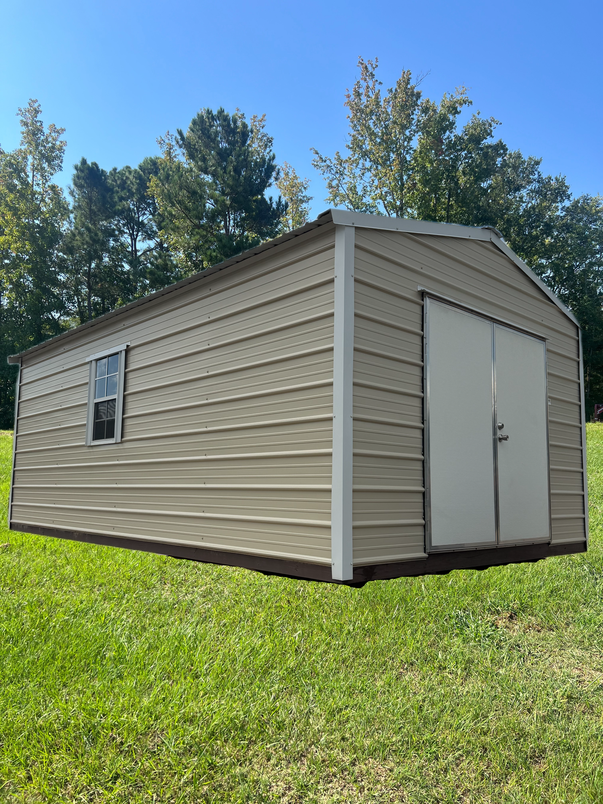 Tan beige storage shed with white trim on a grassy lawn under a blue sky.