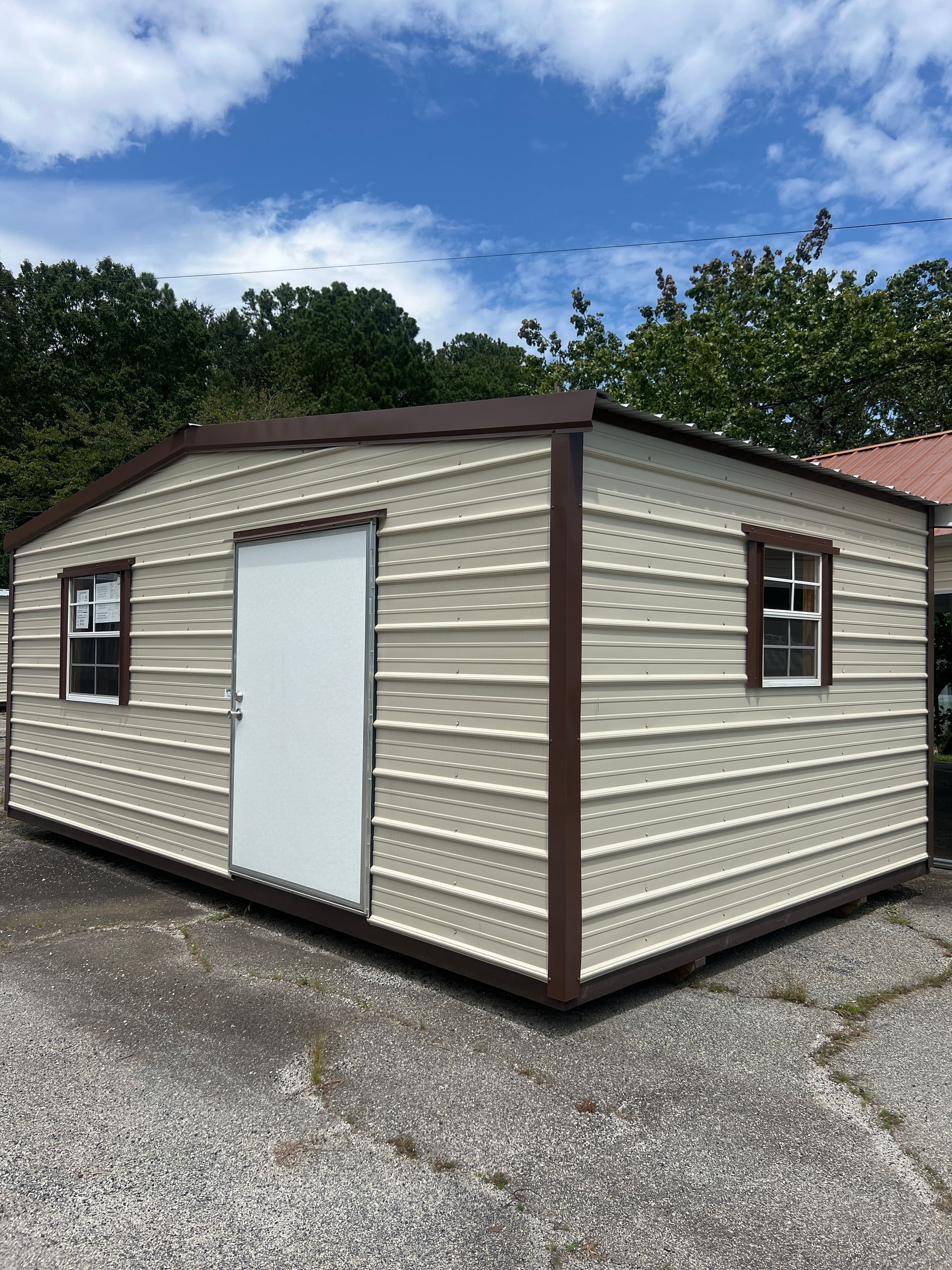 Tan and brown metal shed with a white door and two small windows under a blue sky.
