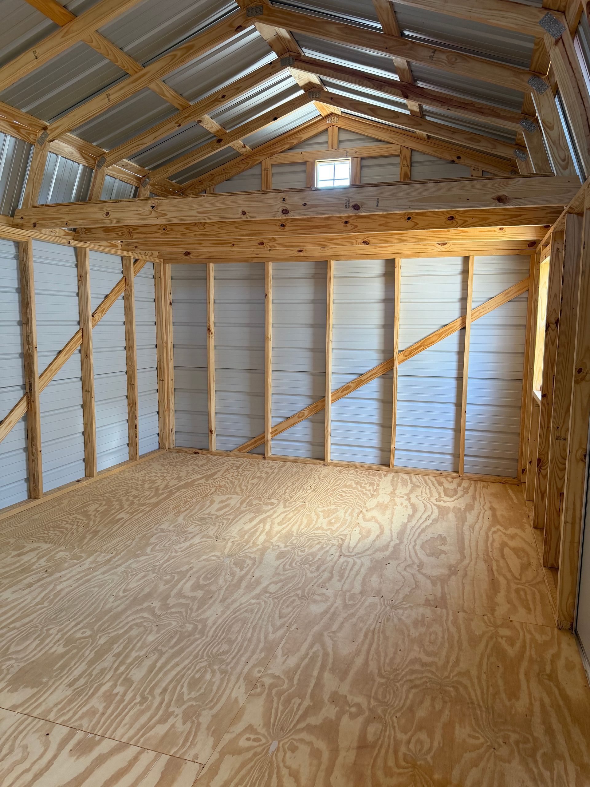 Empty wooden loft interior with plywood floor and exposed rafters under a pitched roof.