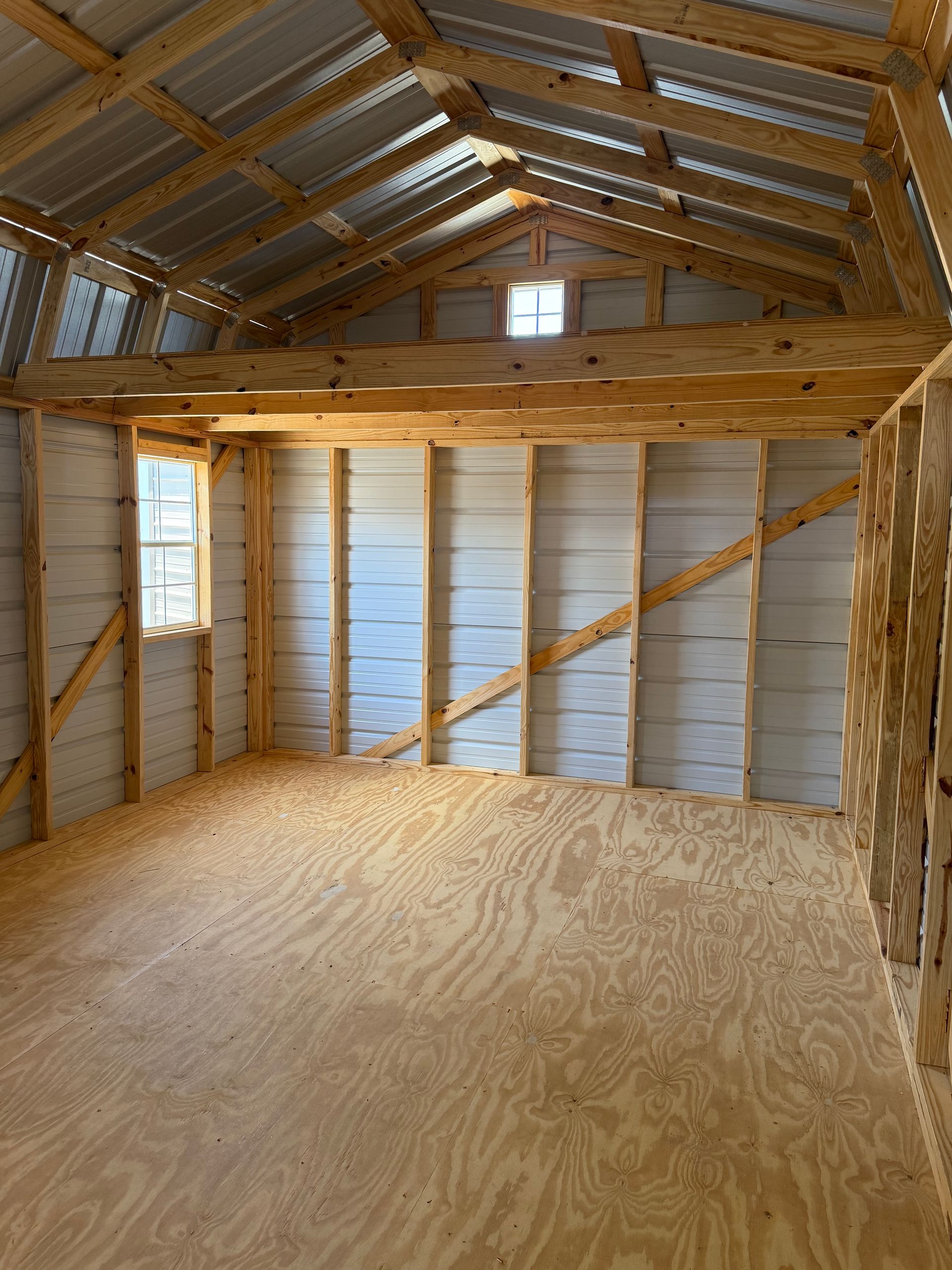 Empty unfinished wooden shed interior with plywood floor, exposed rafters, and insulated walls